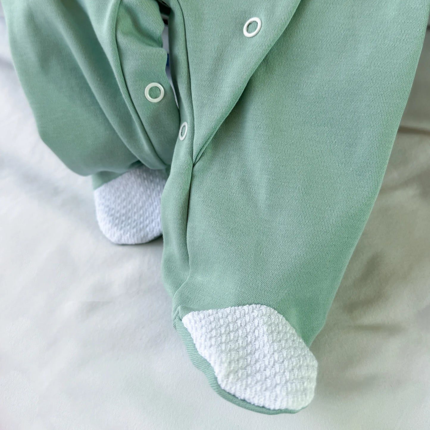 Pormenor de babygrow de algodão com motivo coelhinho e ursinho com livro verde