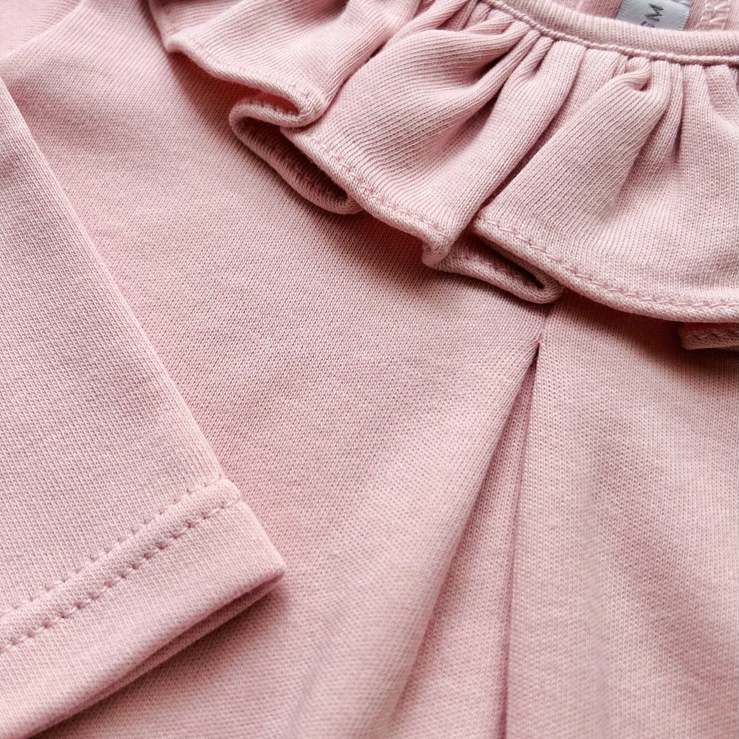 Pormenor de camisola de menina com folho na gola e prega na frente rosa