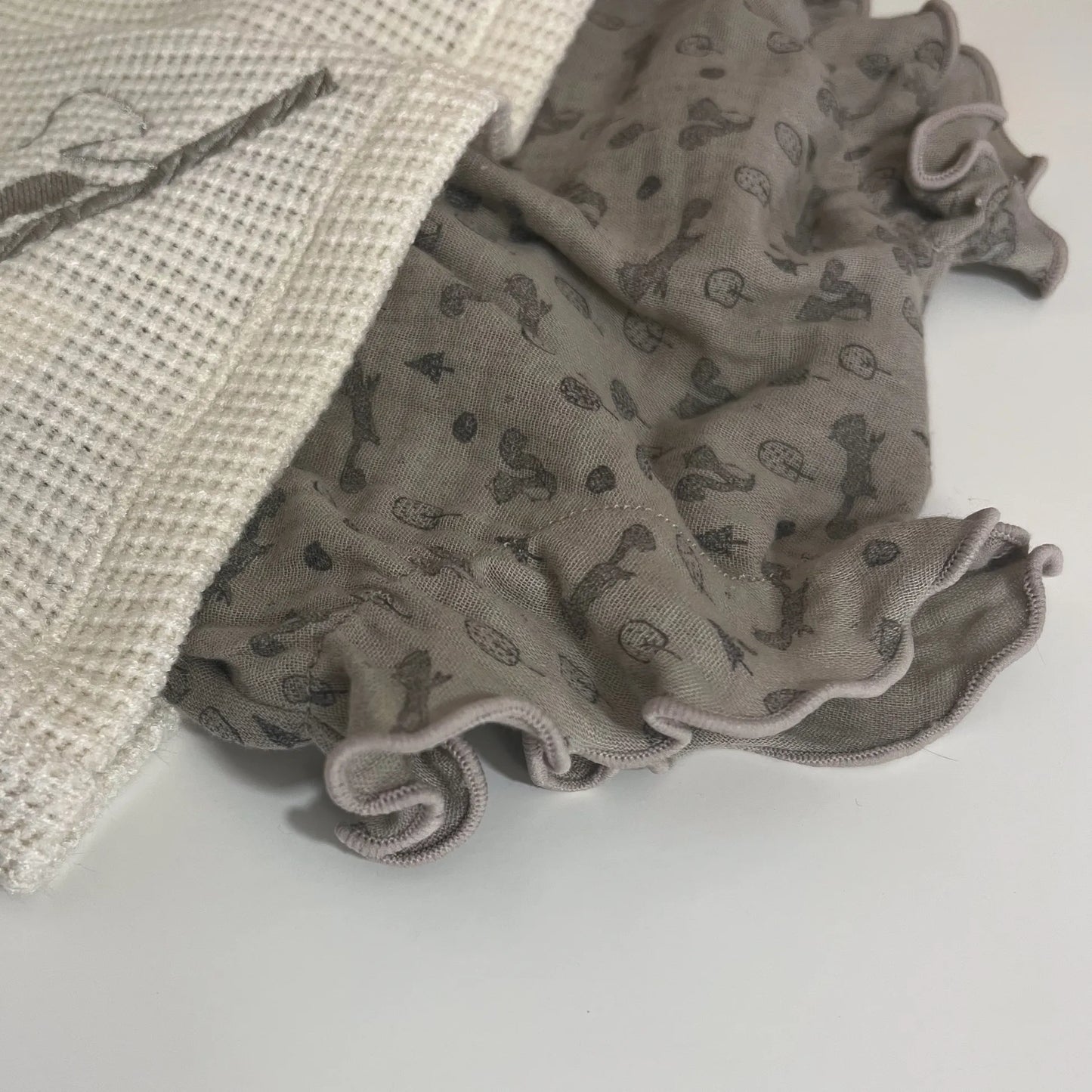 Pormenor de conjunto de menina de camisola pérola com folho na gola e tapa-fraldas cinza