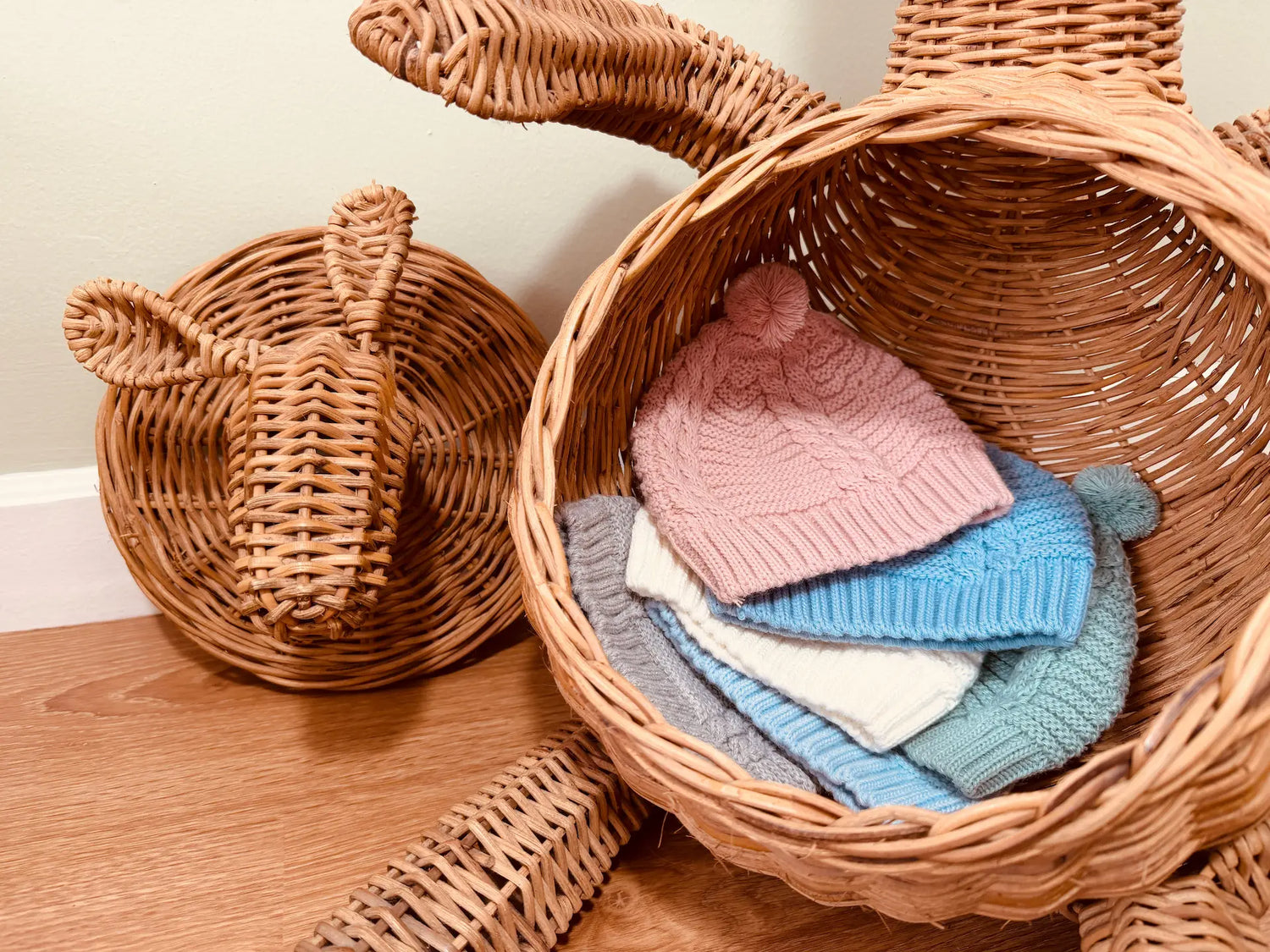 Seis variantes do gorro de malha tricotada com pompom nas cores rosa, cobalto, pérola, verde, azul e cinza dentro da barriga de um coelho grande de verga