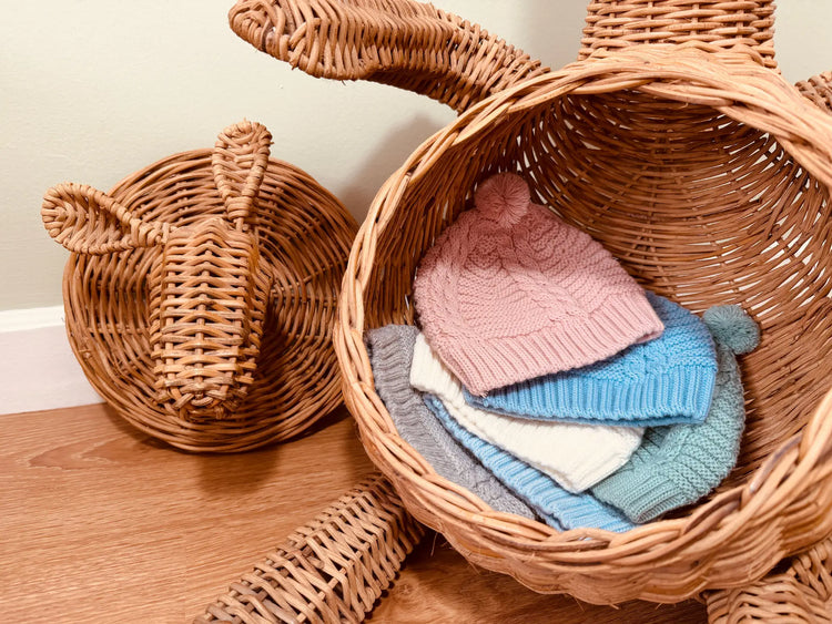 Seis variantes do gorro de malha tricotada com pompom nas cores rosa, cobalto, pérola, verde, azul e cinza dentro da barriga de um coelho grande de verga