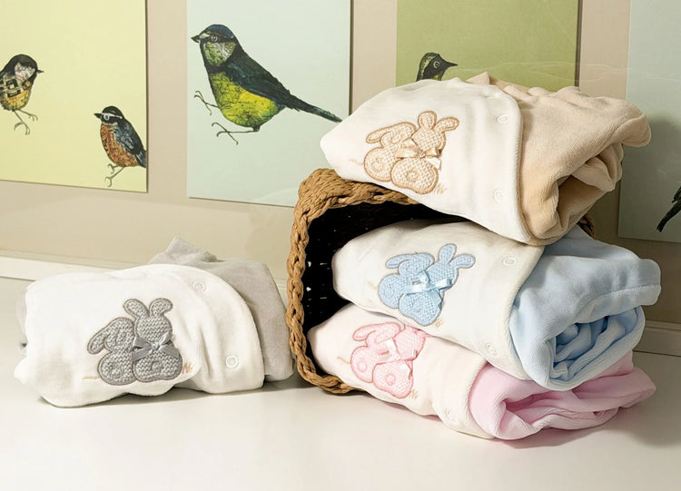 Quatro variantes de babygrow com motivo coelhos tricot com laço nas cores cinza, bege, azul e rosa empilhados