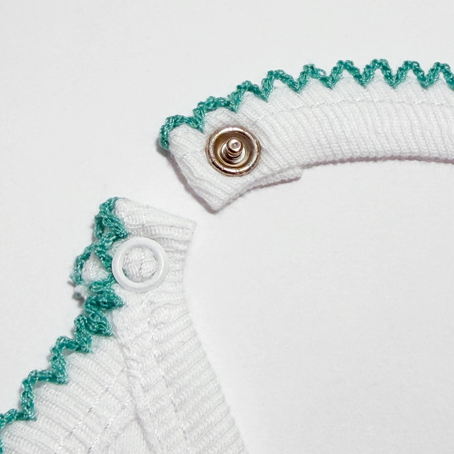 Pormenor de babete com motivo coelhinhos abraçados verde