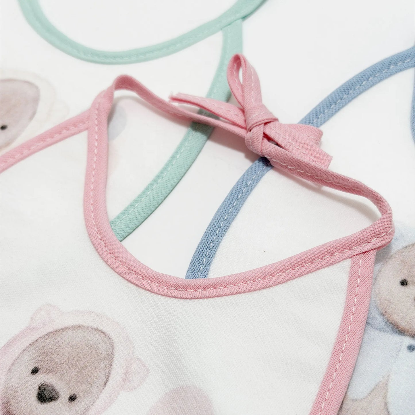 Pormenor de babetes com motivo ursinho com capuz verde, rosa e azul