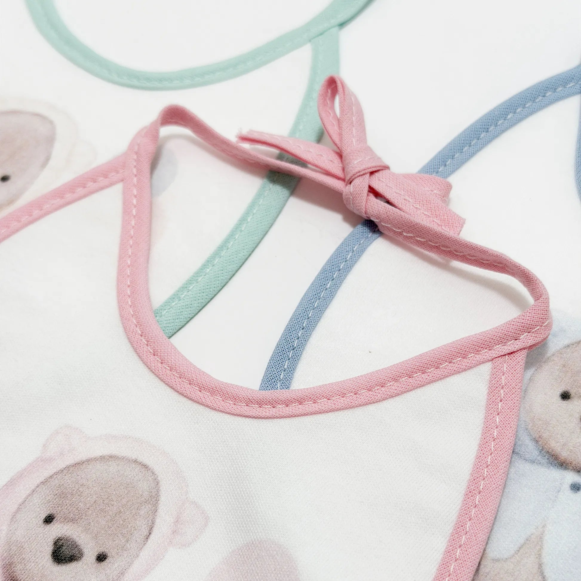 Pormenor de babetes com motivo ursinho com capuz verde, rosa e azul