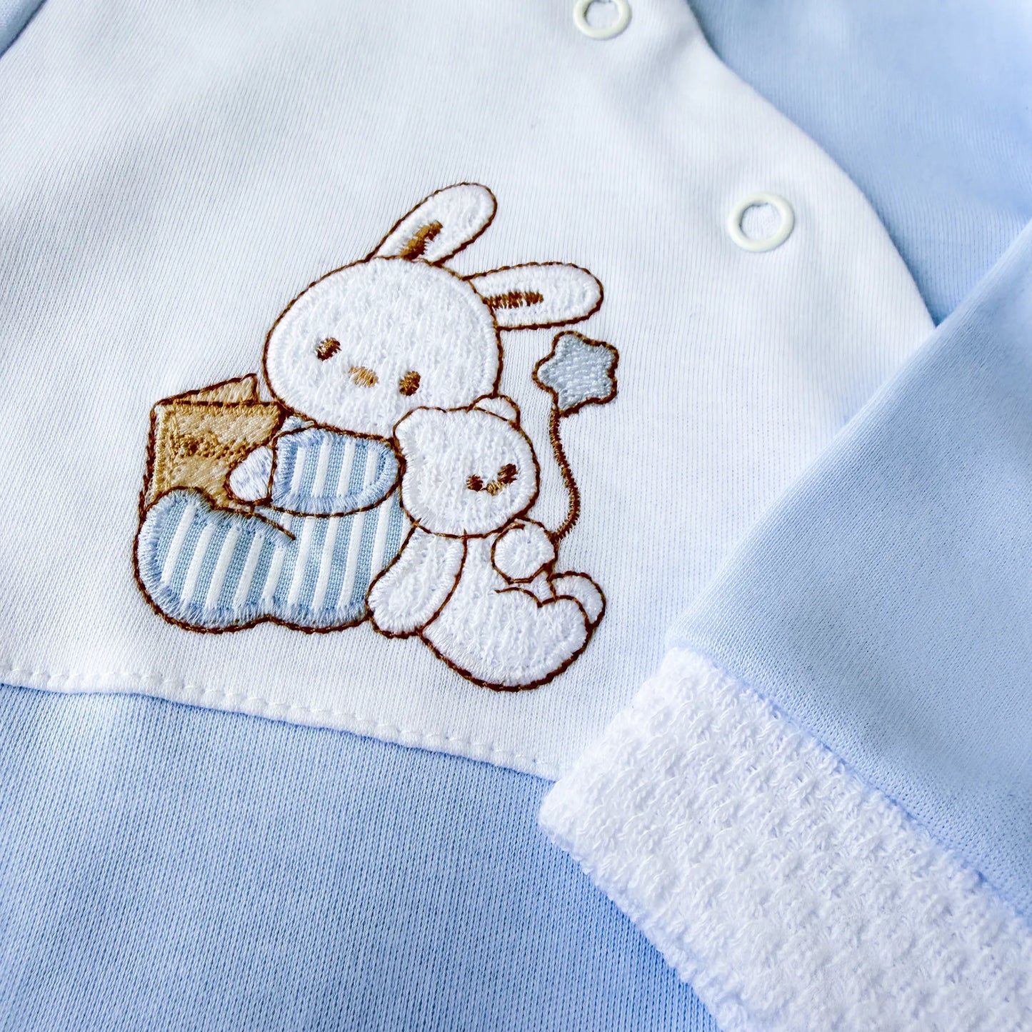 Pormenor de babygrow de algodão com motivo coelhinho e ursinho com livro azul