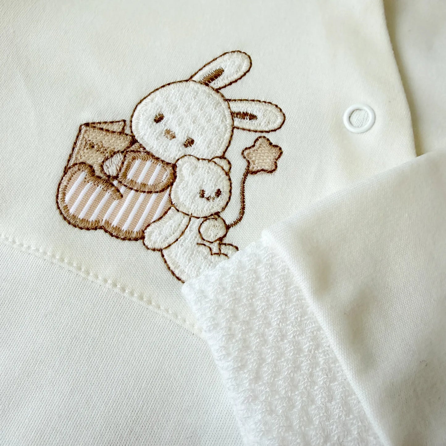 Pormenor de babygrow de algodão com motivo coelhinho e ursinho com livro pérola