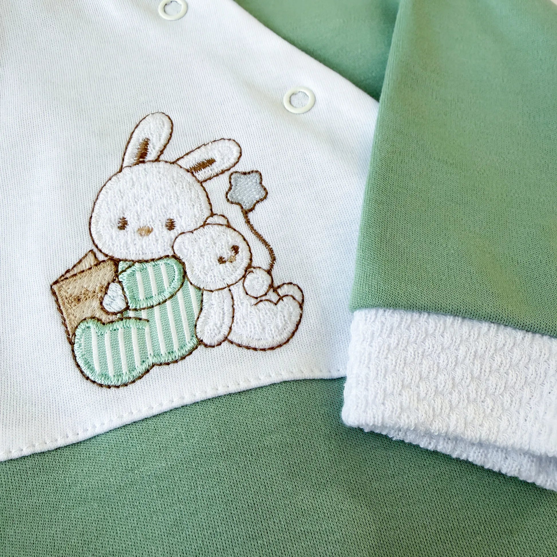 Pormenor de babygrow de algodão com motivo coelhinho e ursinho com livro verde