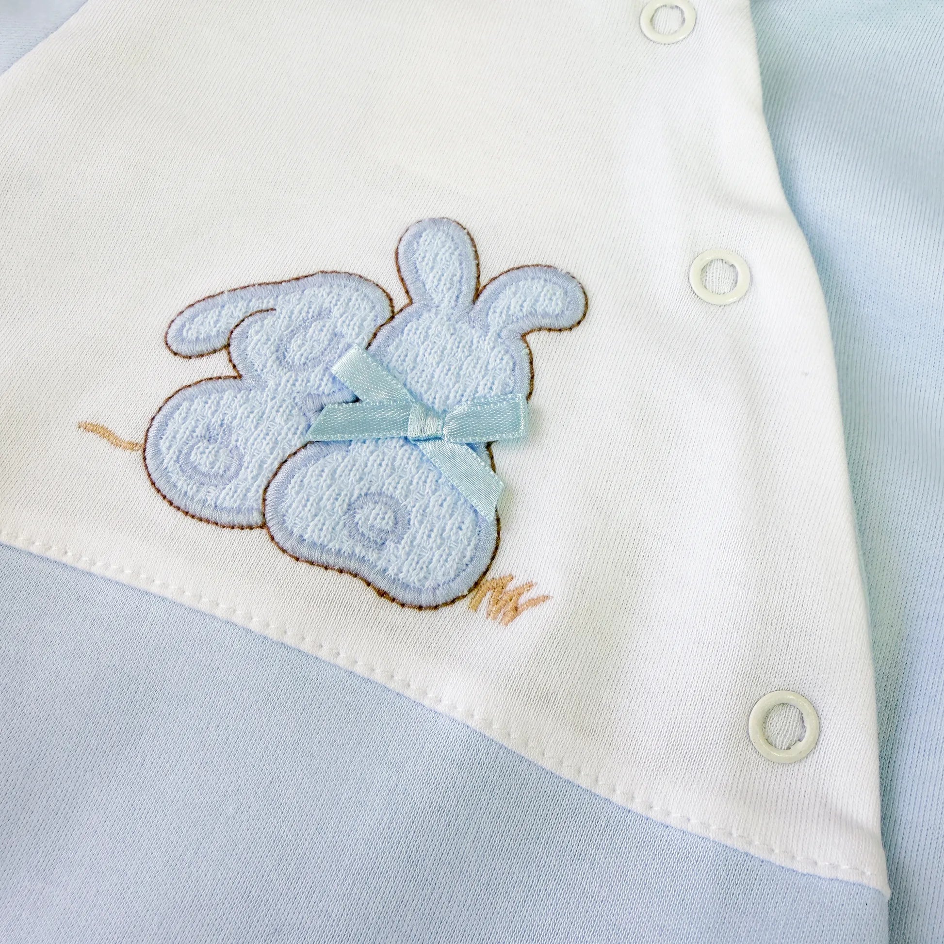 Pormenor de babygrow de algodão com motivo coelhos tricot com lacinho azul