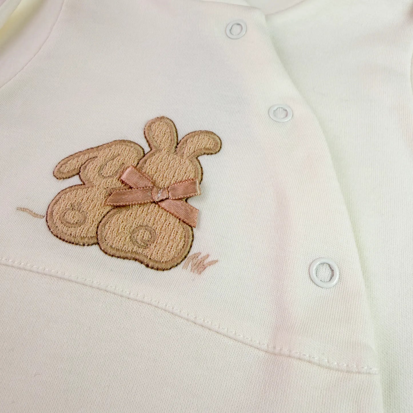 Pormenor de babygrow de algodão com motivo coelhos tricot com lacinho pérola
