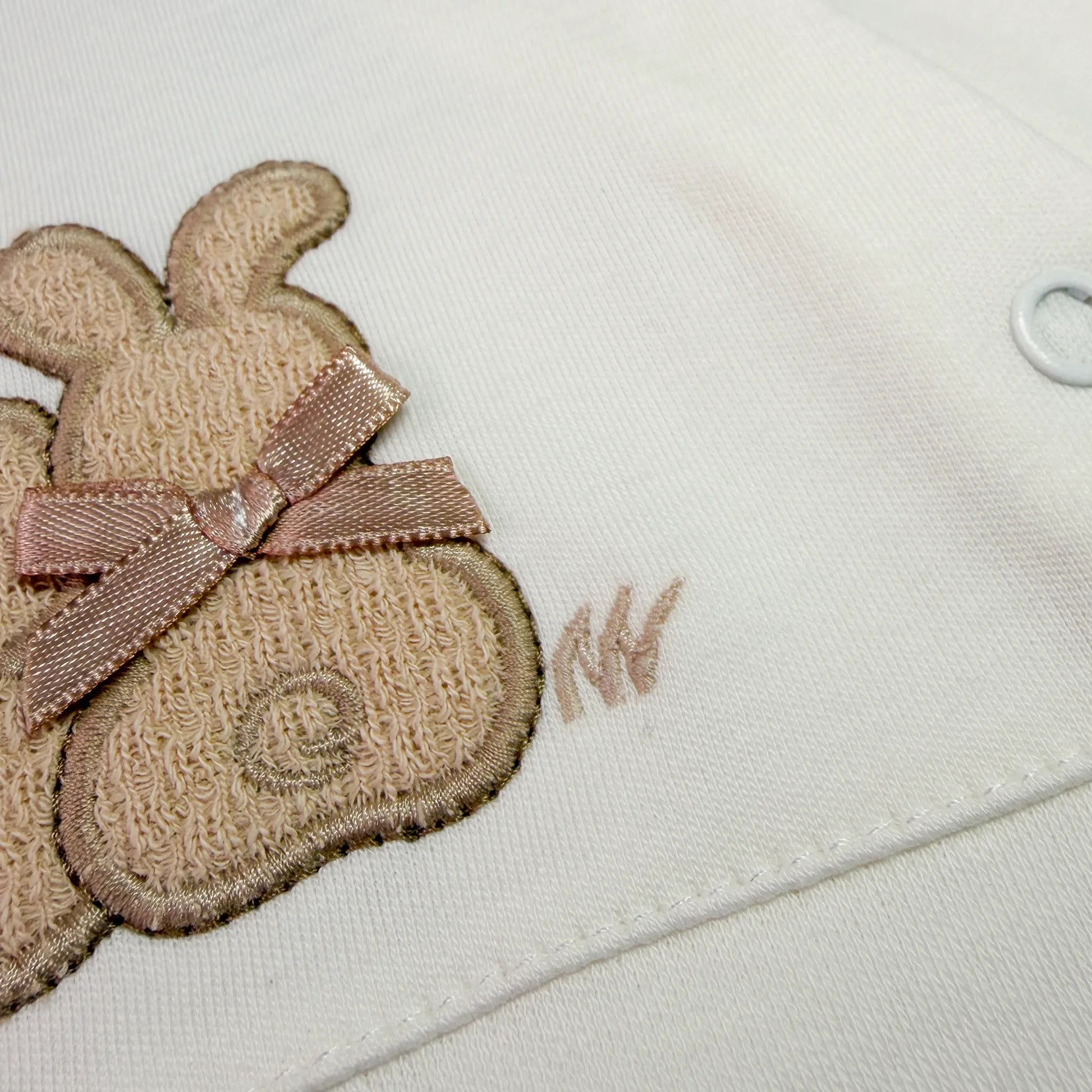 Pormenor de babygrow de algodão com motivo coelhos tricot com lacinho pérola