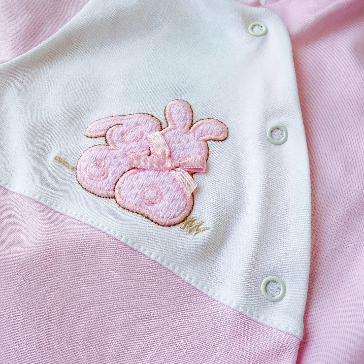 Pormenor de babygrow de algodão com motivo coelhos tricot com lacinho rosa