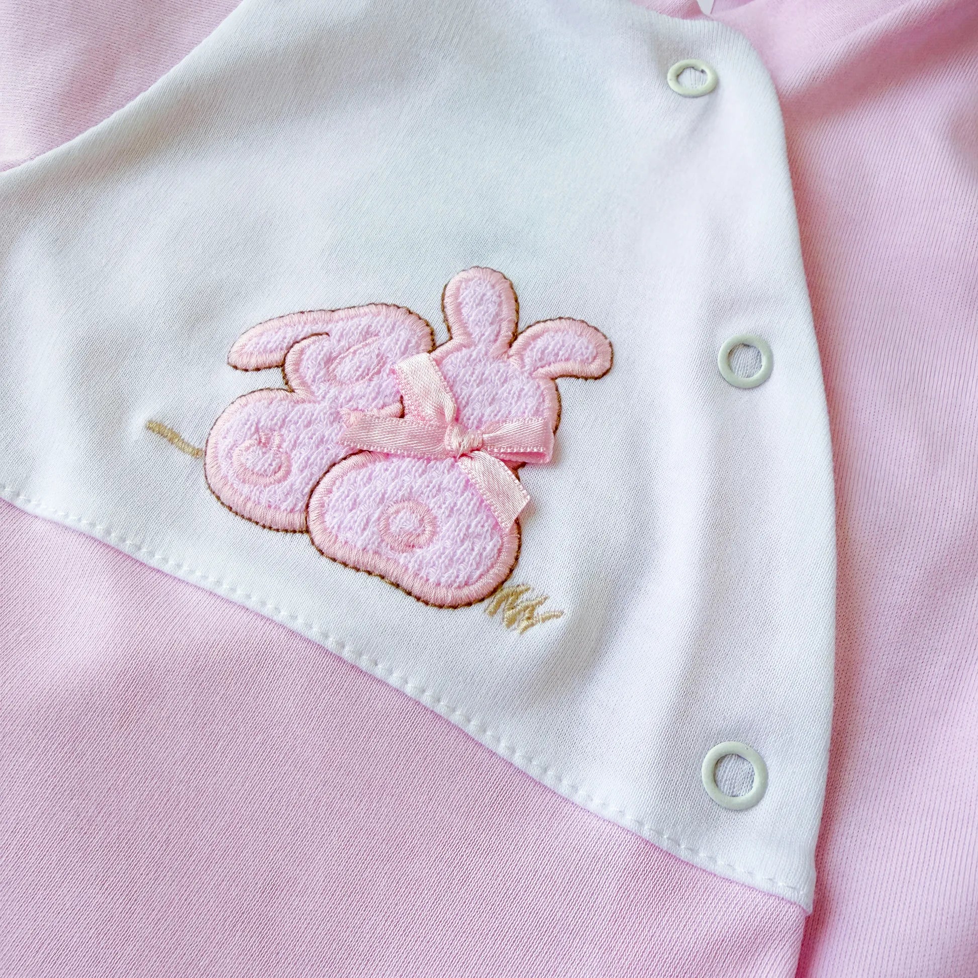 Pormenor de babygrow de algodão com motivo coelhos tricot com lacinho rosa