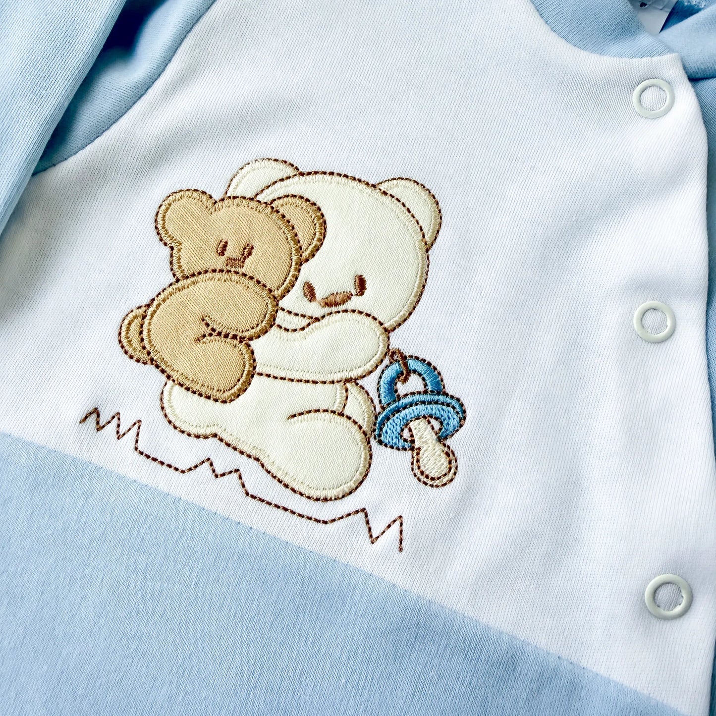 Pormenor de babygrow de algodão com motivo ursinho às cavalitas azul