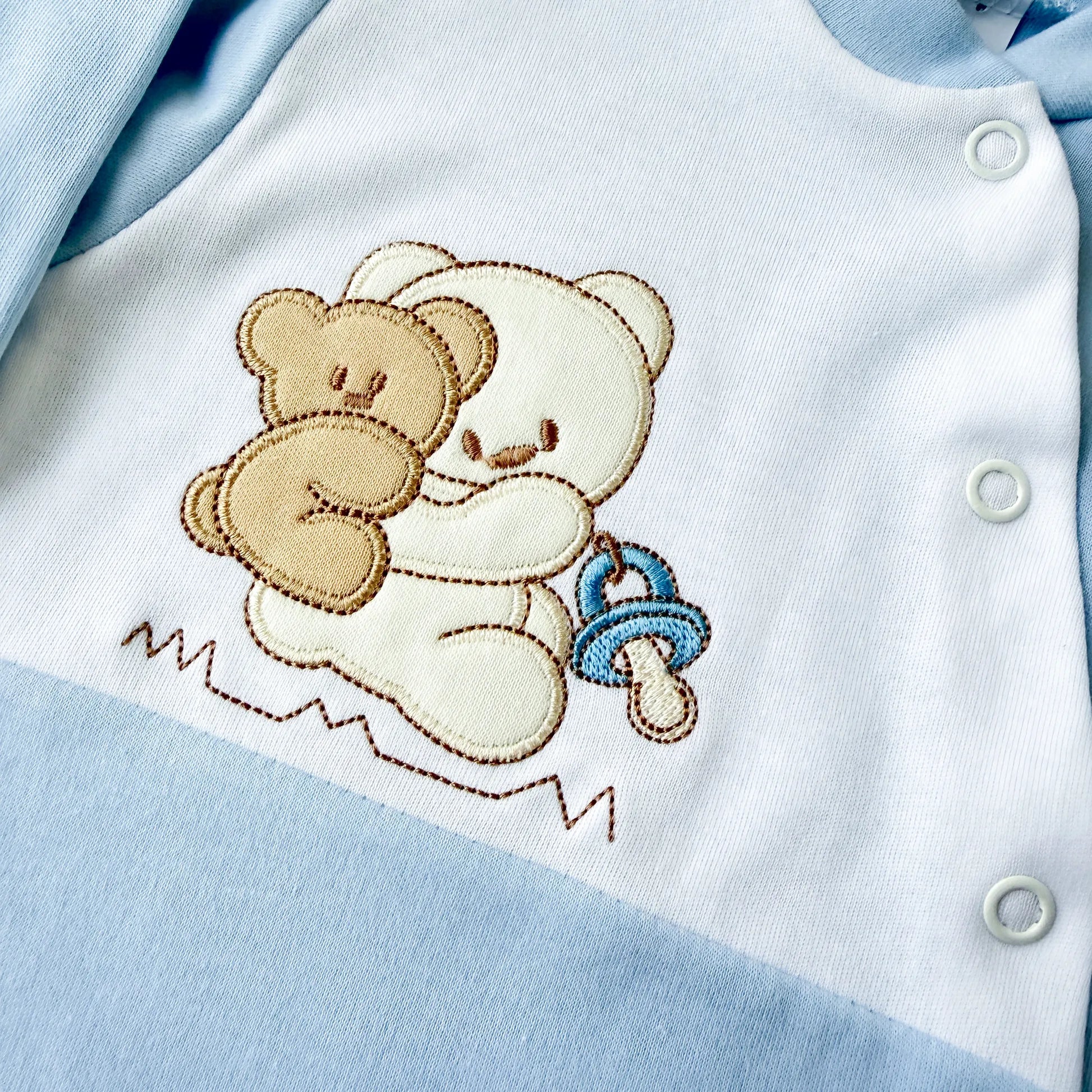 Pormenor de babygrow de algodão com motivo ursinho às cavalitas azul