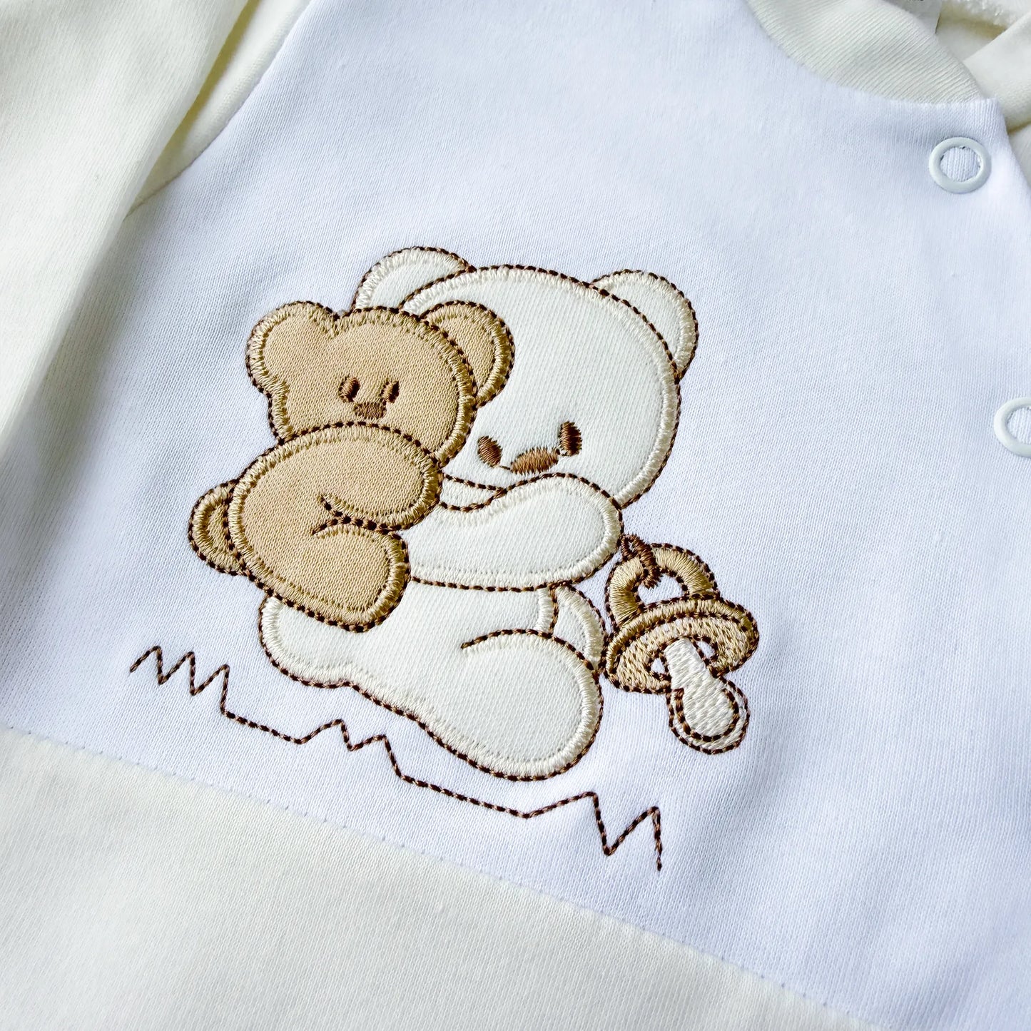 Pormenor de babygrow de algodão com motivo ursinho às cavalitas pérola