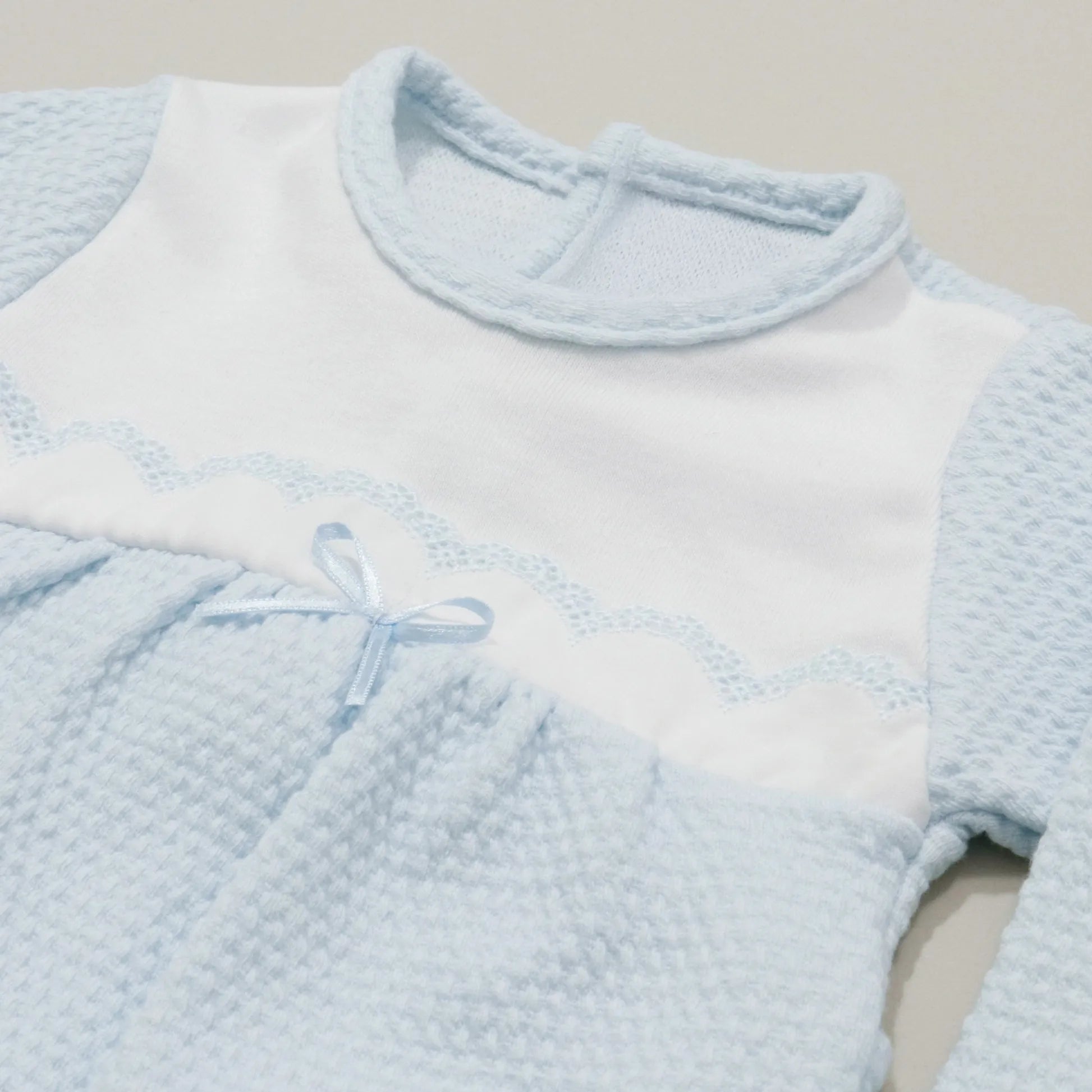 Pormenor de babygrow com efeito renda e lacinho no peito azul