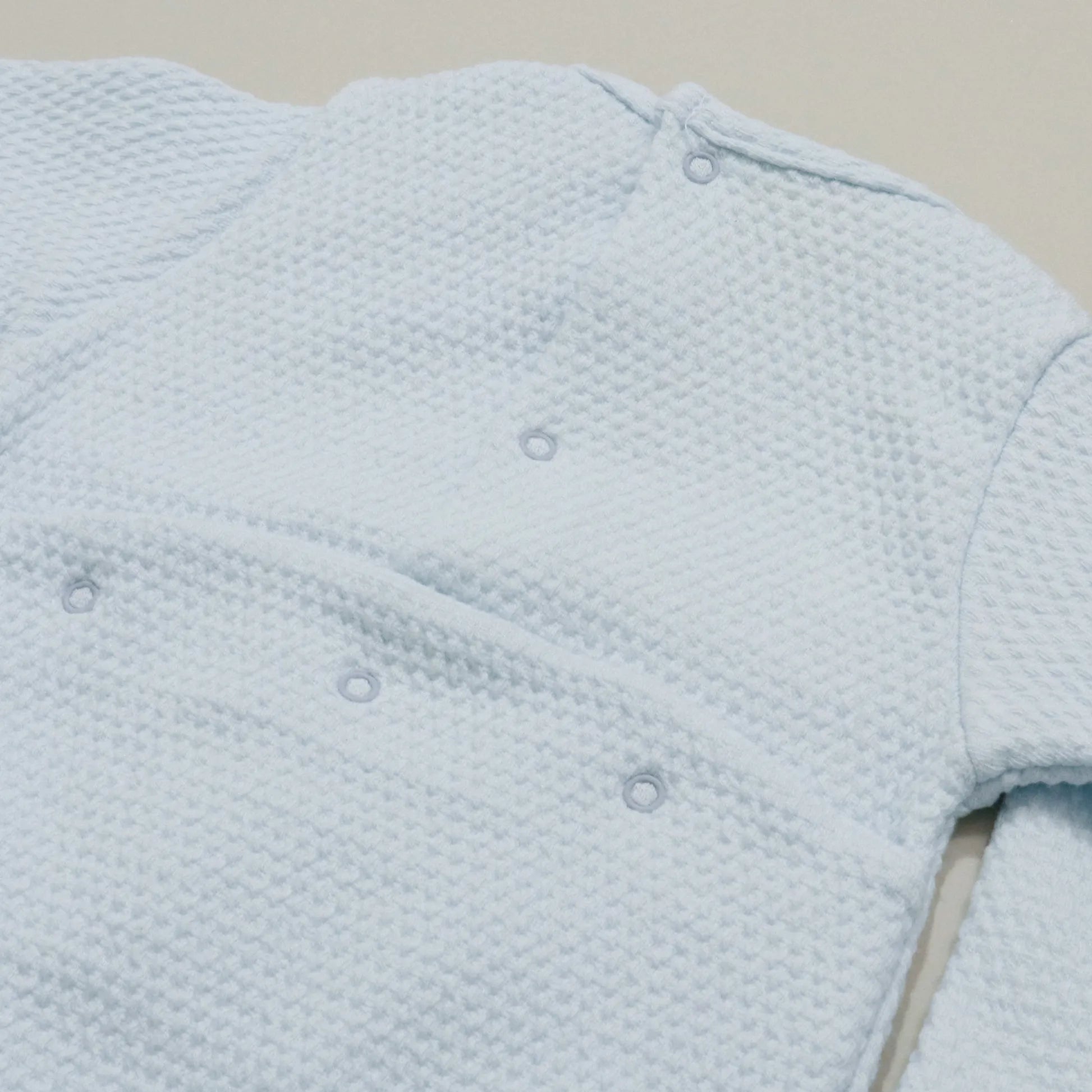 Pormenor de babygrow com efeito renda e lacinho no peito azul