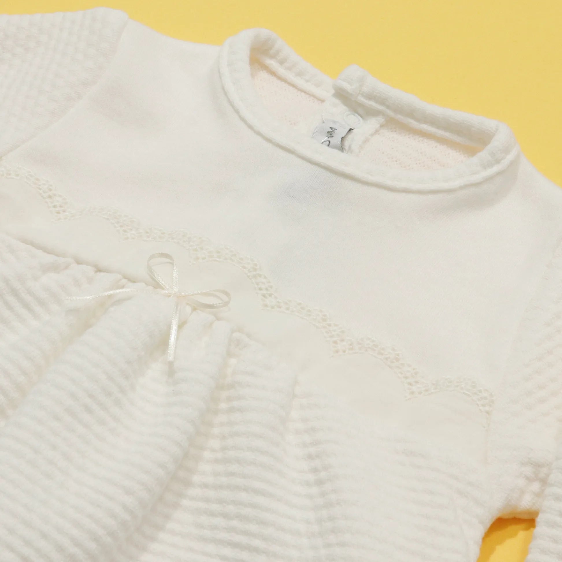 Pormenor de babygrow com efeito renda e lacinho no peito pérola