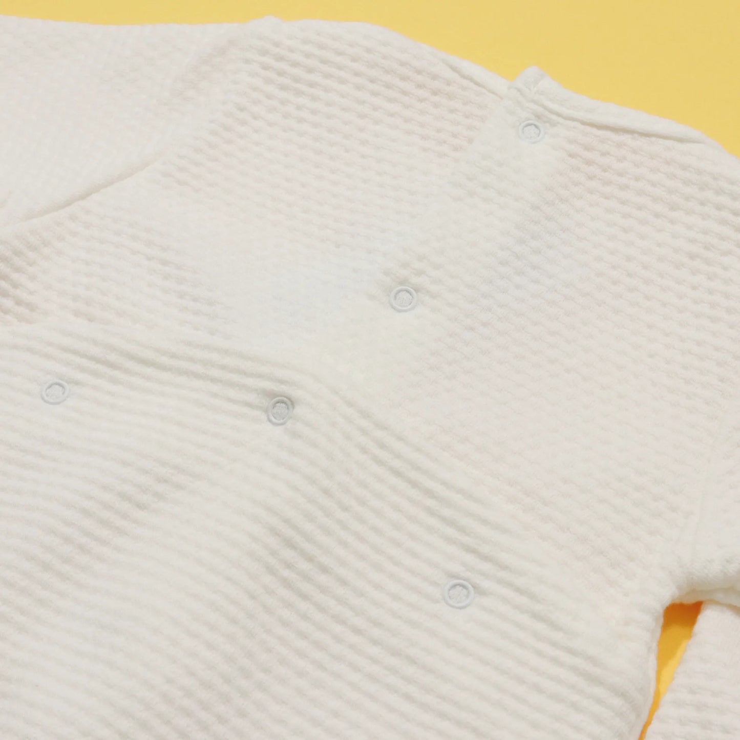 Pormenor de babygrow com efeito renda e lacinho no peito pérola