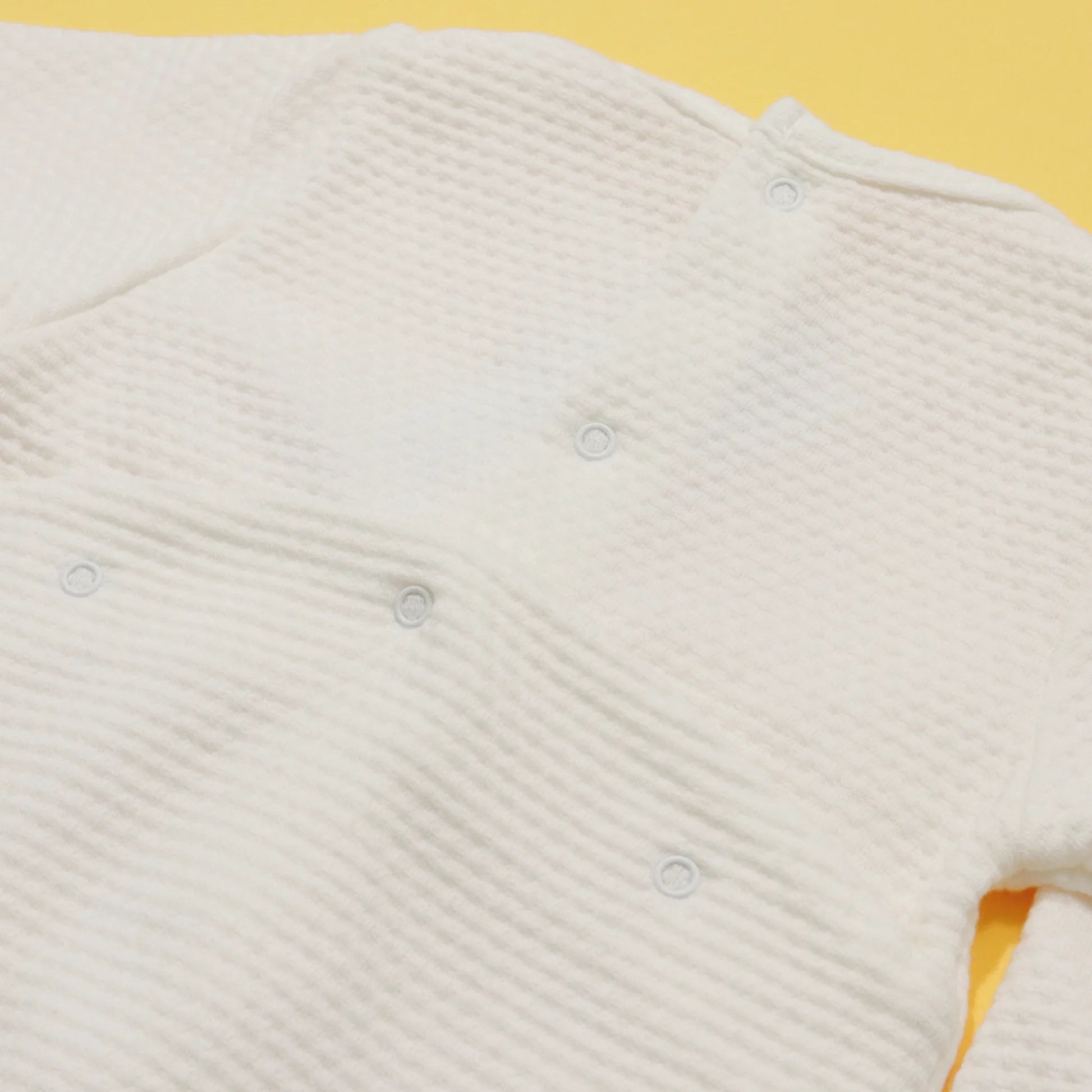Pormenor de babygrow com efeito renda e lacinho no peito pérola