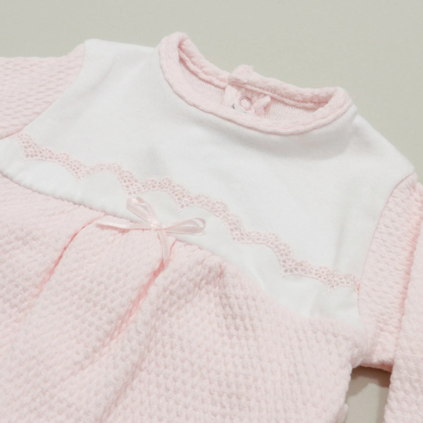 Pormenor de babygrow com efeito renda e lacinho no peito rosa