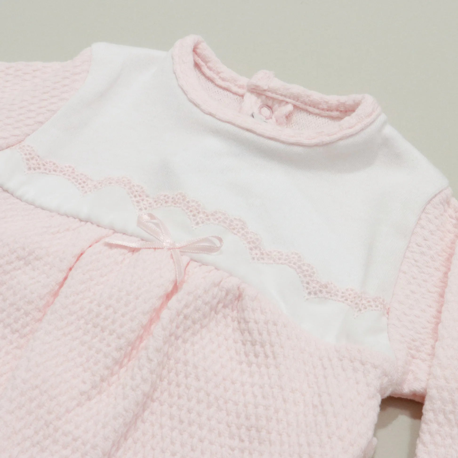 Pormenor de babygrow com efeito renda e lacinho no peito rosa
