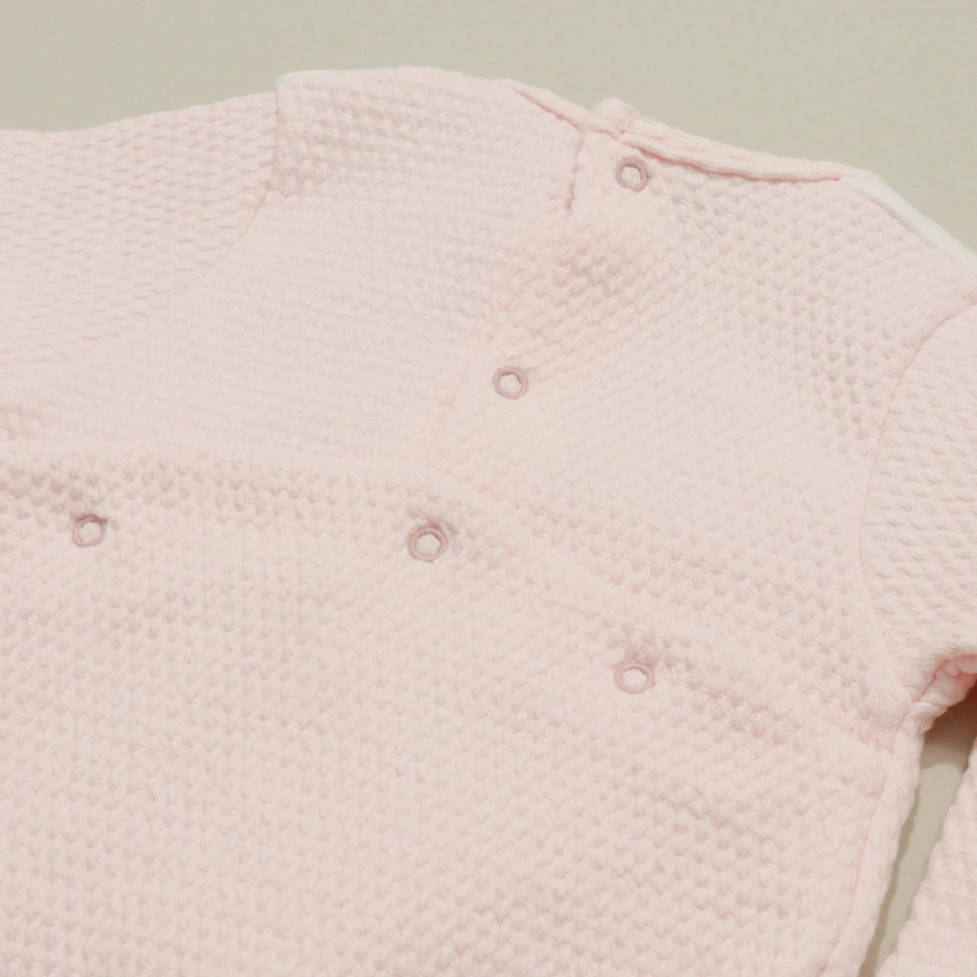 Pormenor de babygrow com efeito renda e lacinho no peito rosa