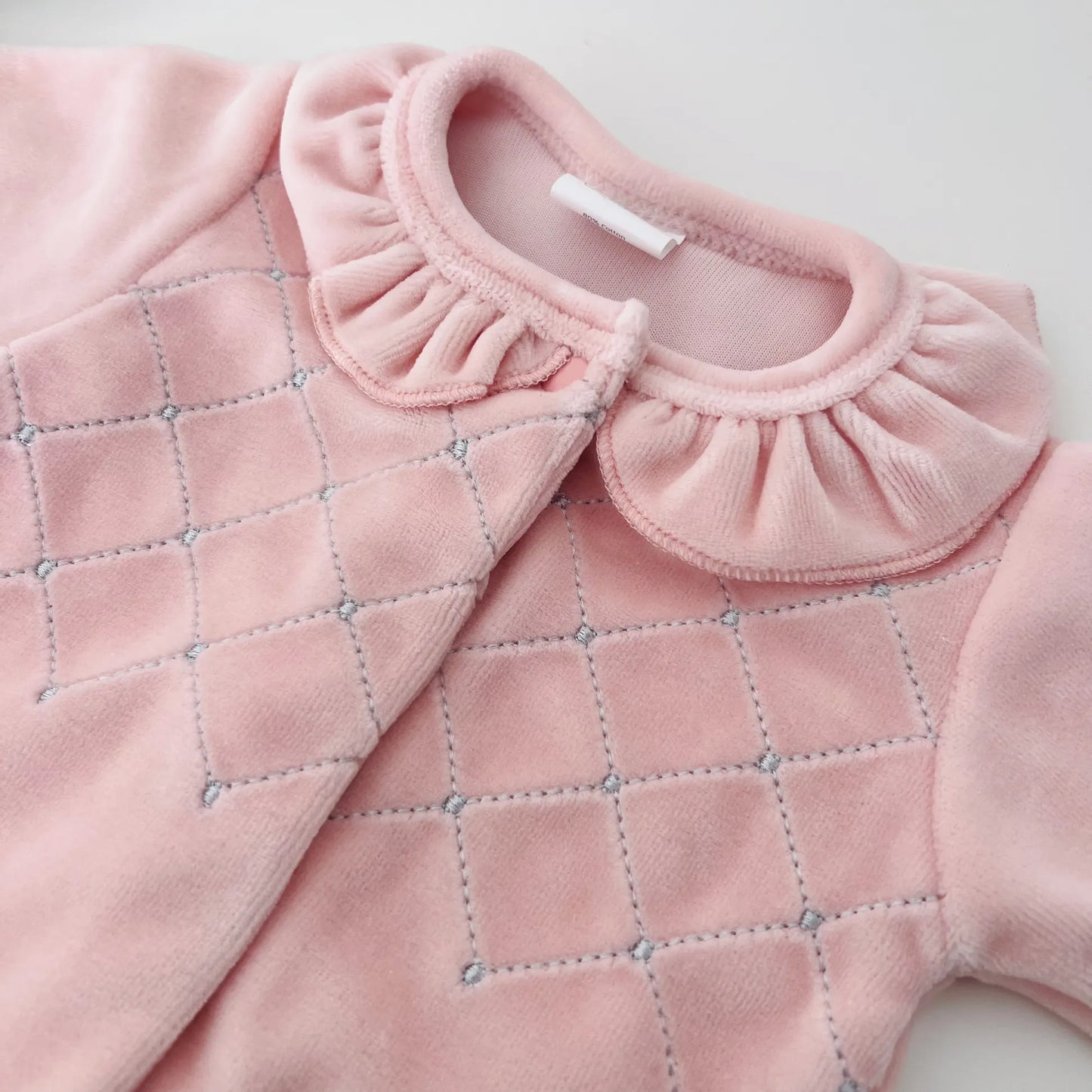 Pormenor de babygrow de menina com gola redonda e bordado losangos rosa