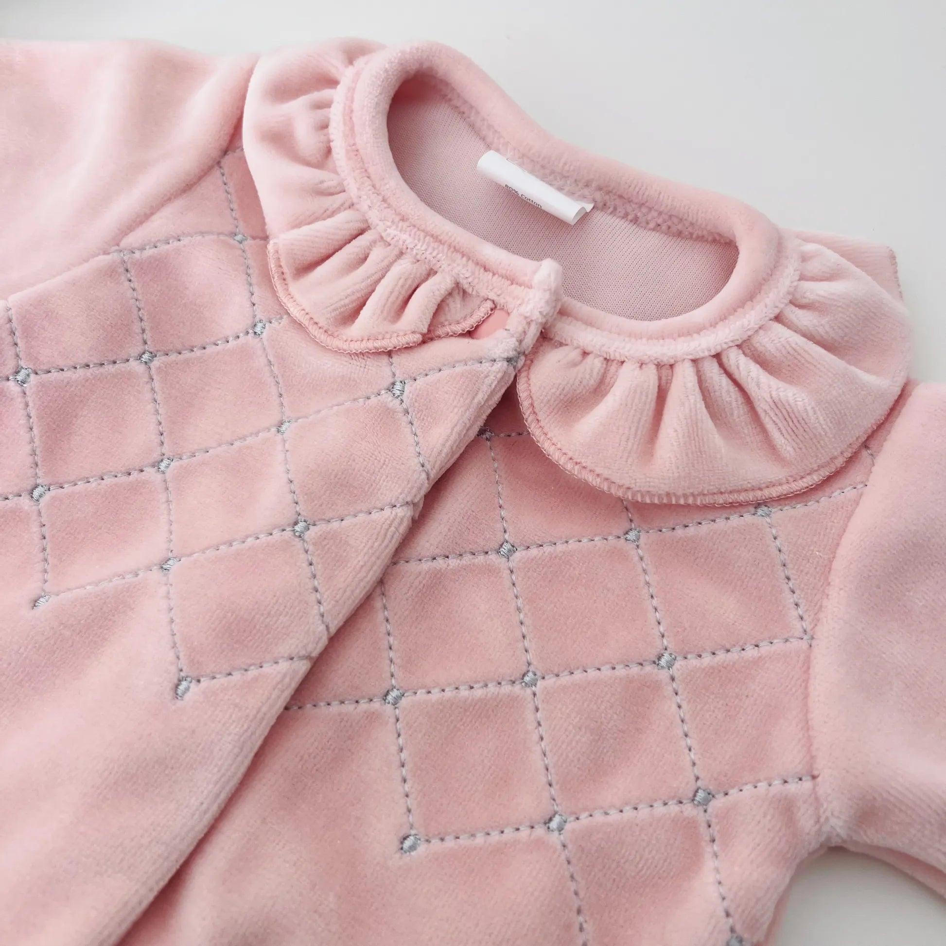 Pormenor de babygrow de menina com gola redonda e bordado losangos rosa