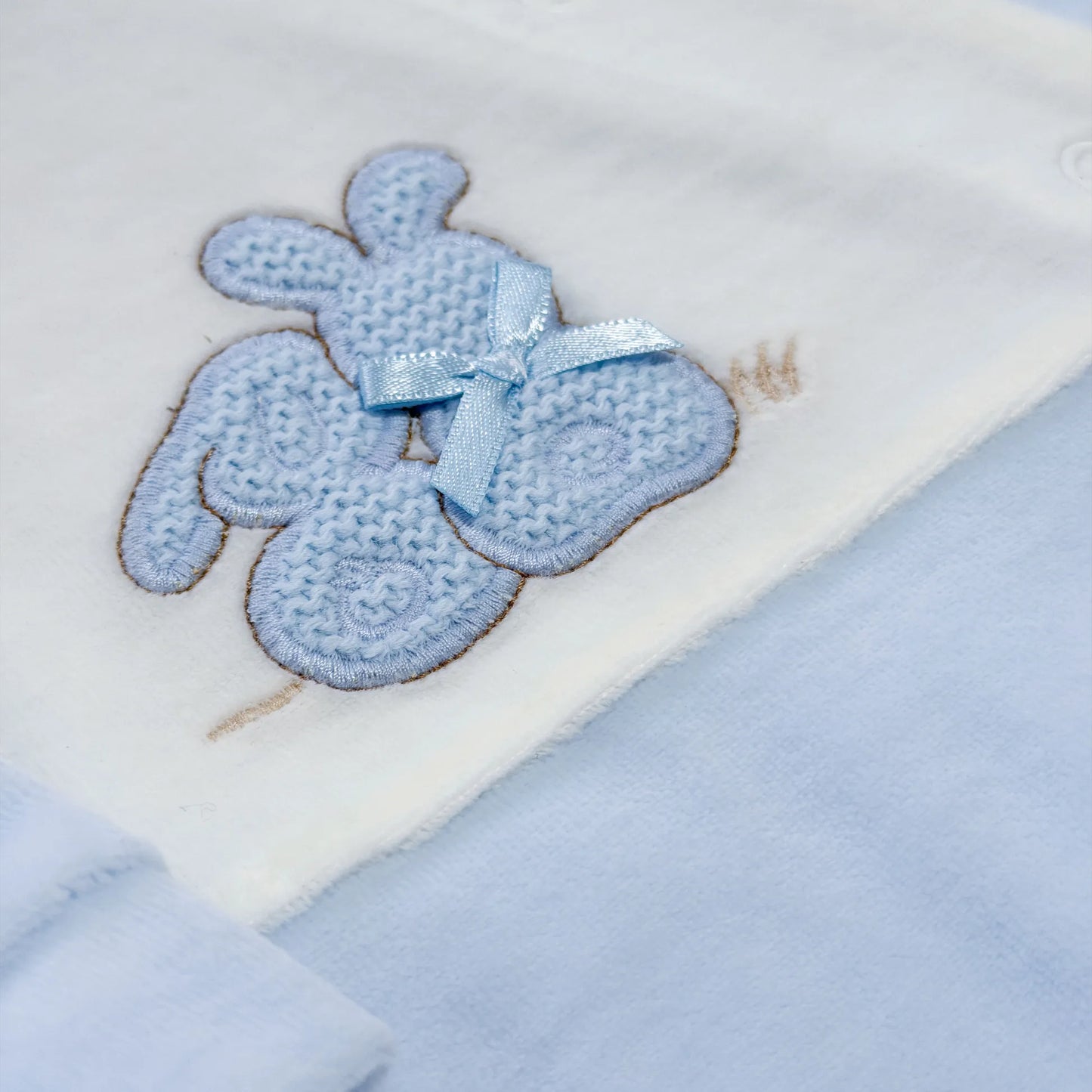 Pormenor de babygrow com motivo coelhos tricot com lacinho azul