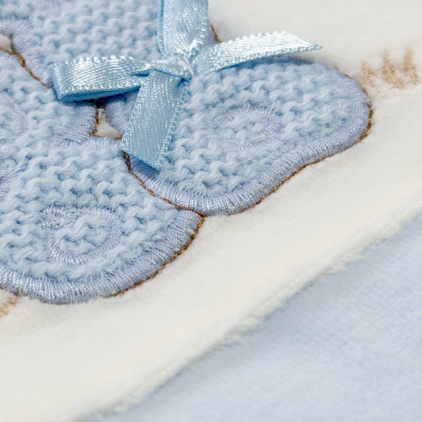 Pormenor de babygrow com motivo coelhos tricot com lacinho azul