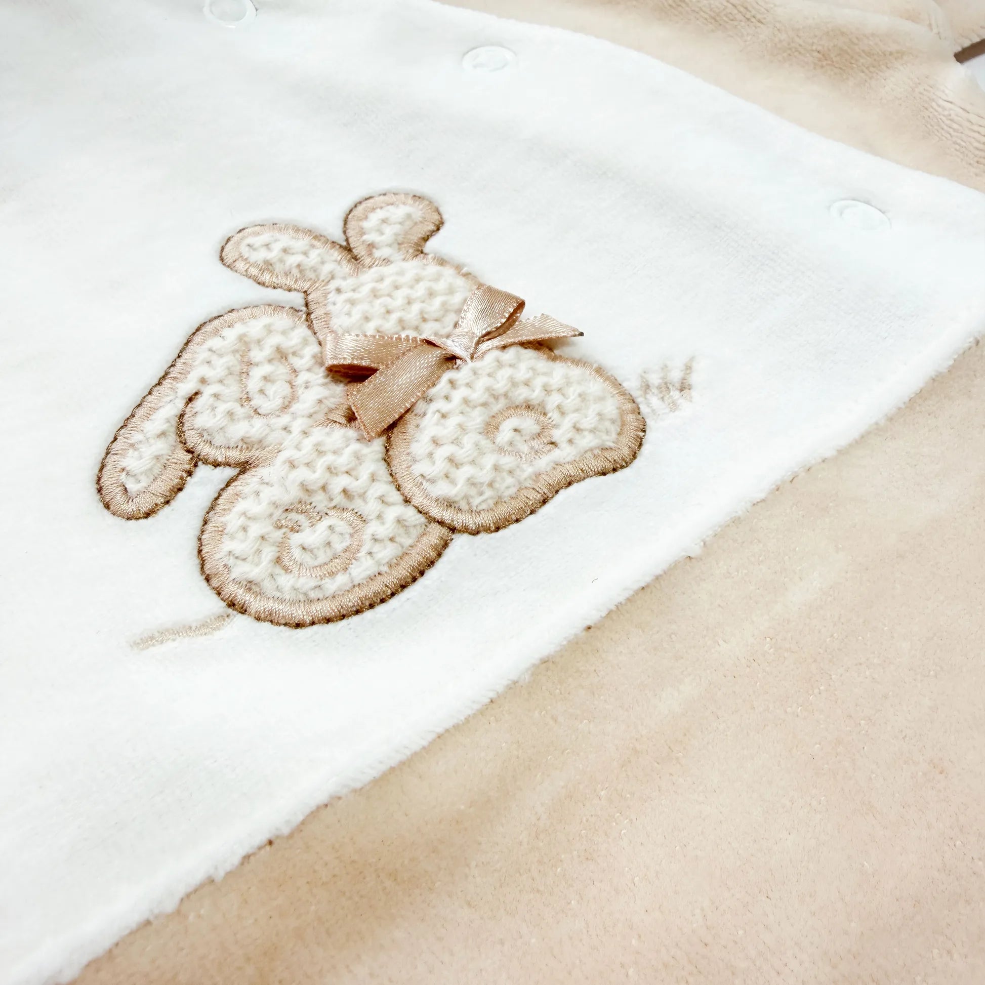 Pormenor de babygrow com motivo coelhos tricot com lacinho bege