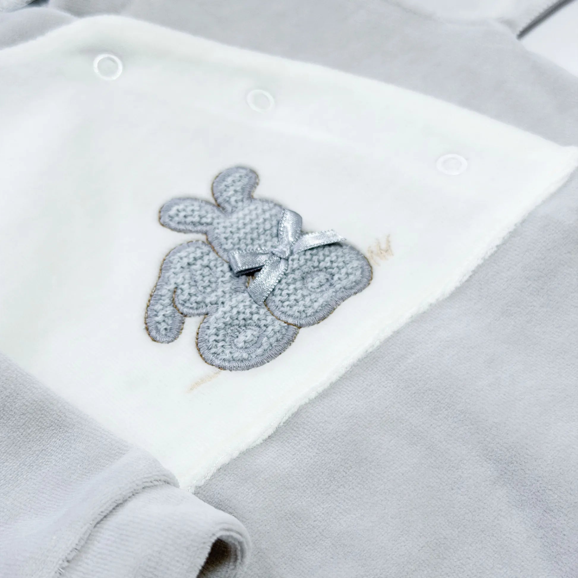 Pormenor de babygrow com motivo coelhos tricot com lacinho cinza