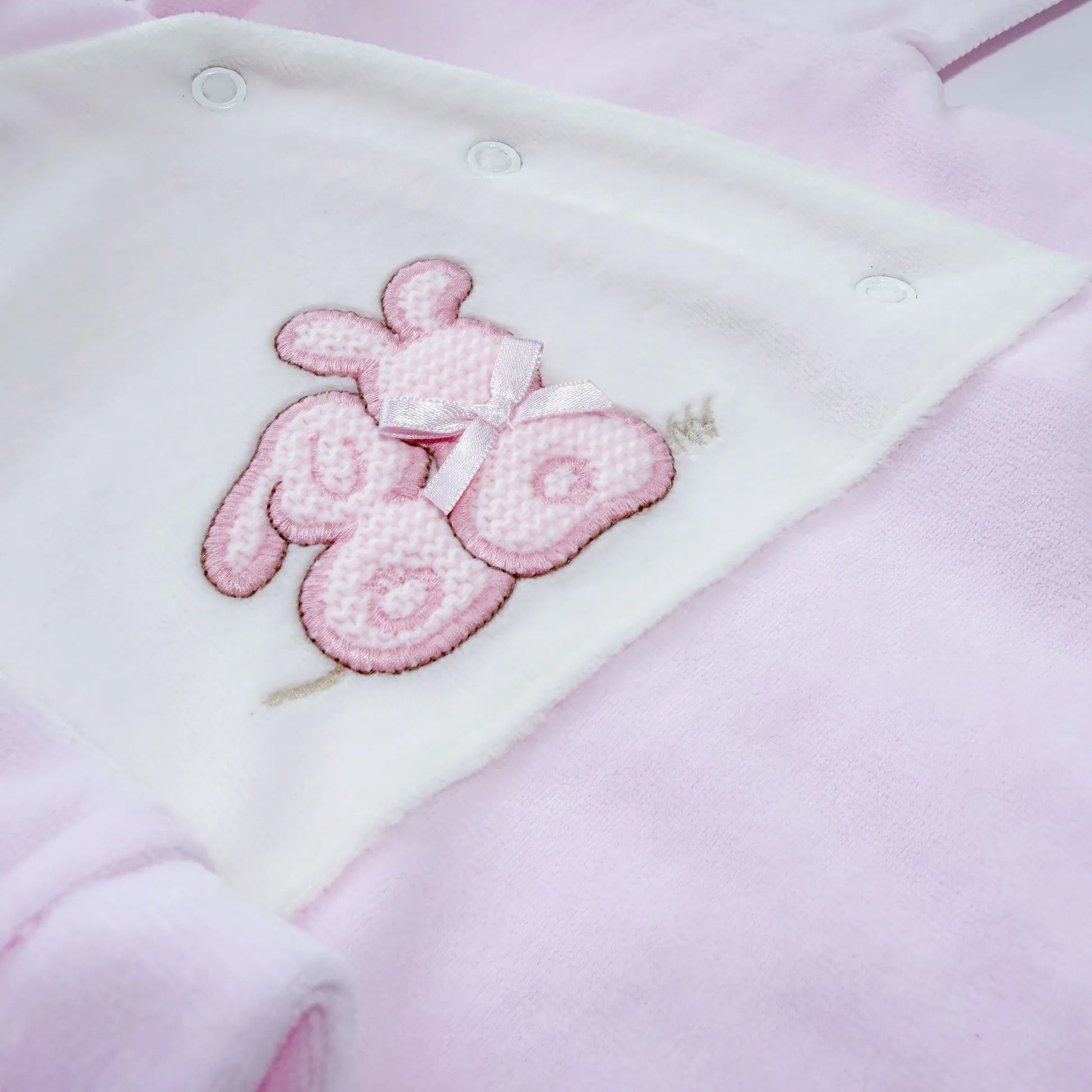Pormenor de babygrow com motivo coelhos tricot com lacinho rosa
