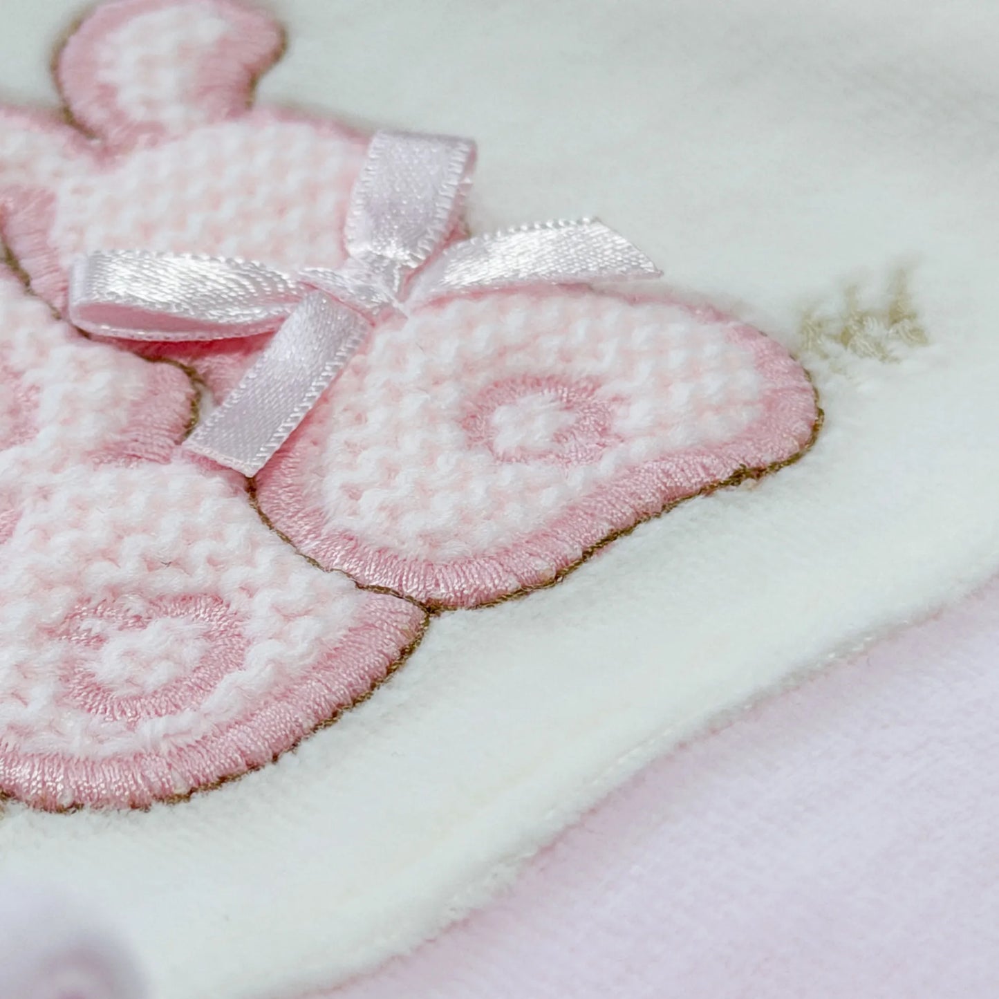 Pormenor de babygrow com motivo coelhos tricot com lacinho rosa