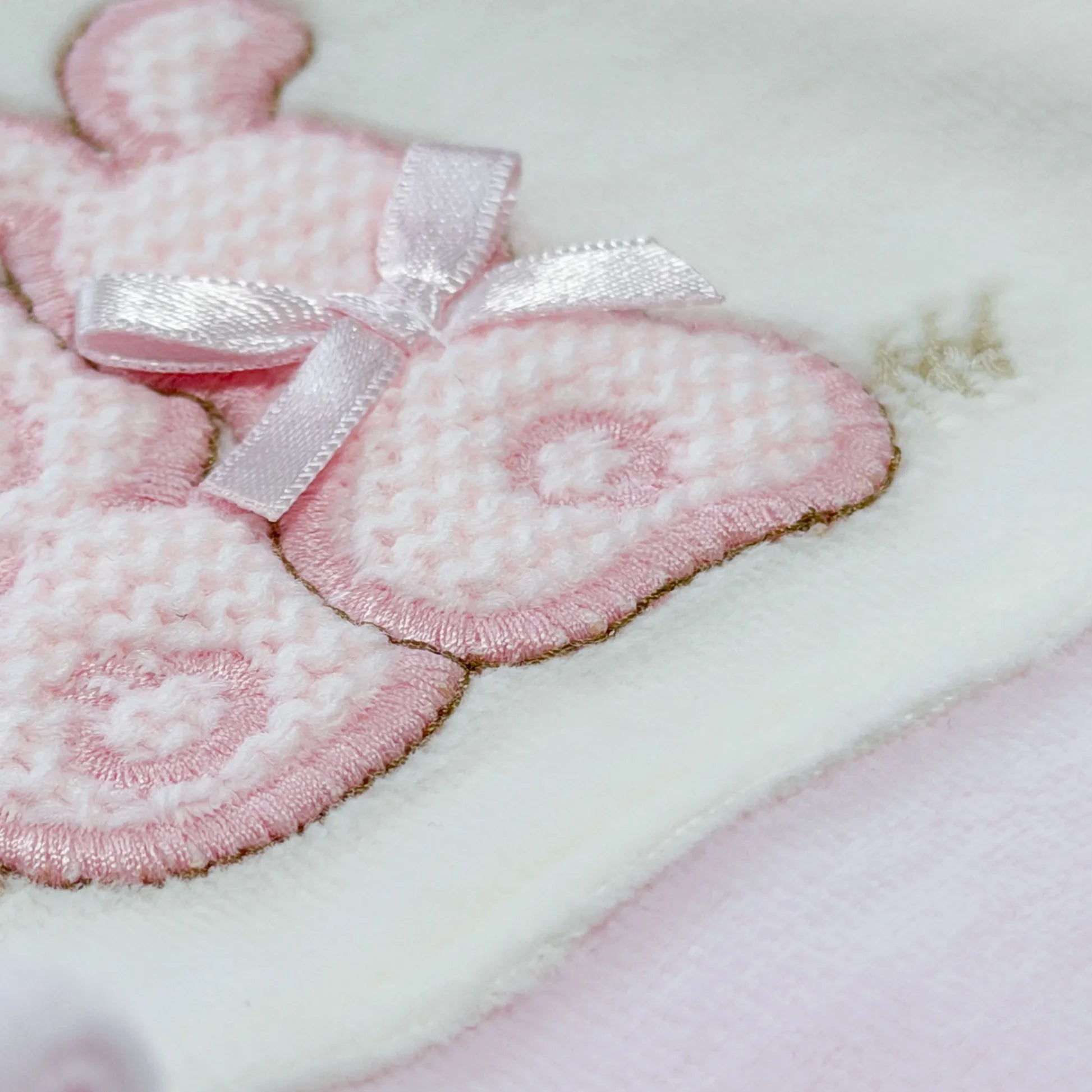 Pormenor de babygrow com motivo coelhos tricot com lacinho rosa
