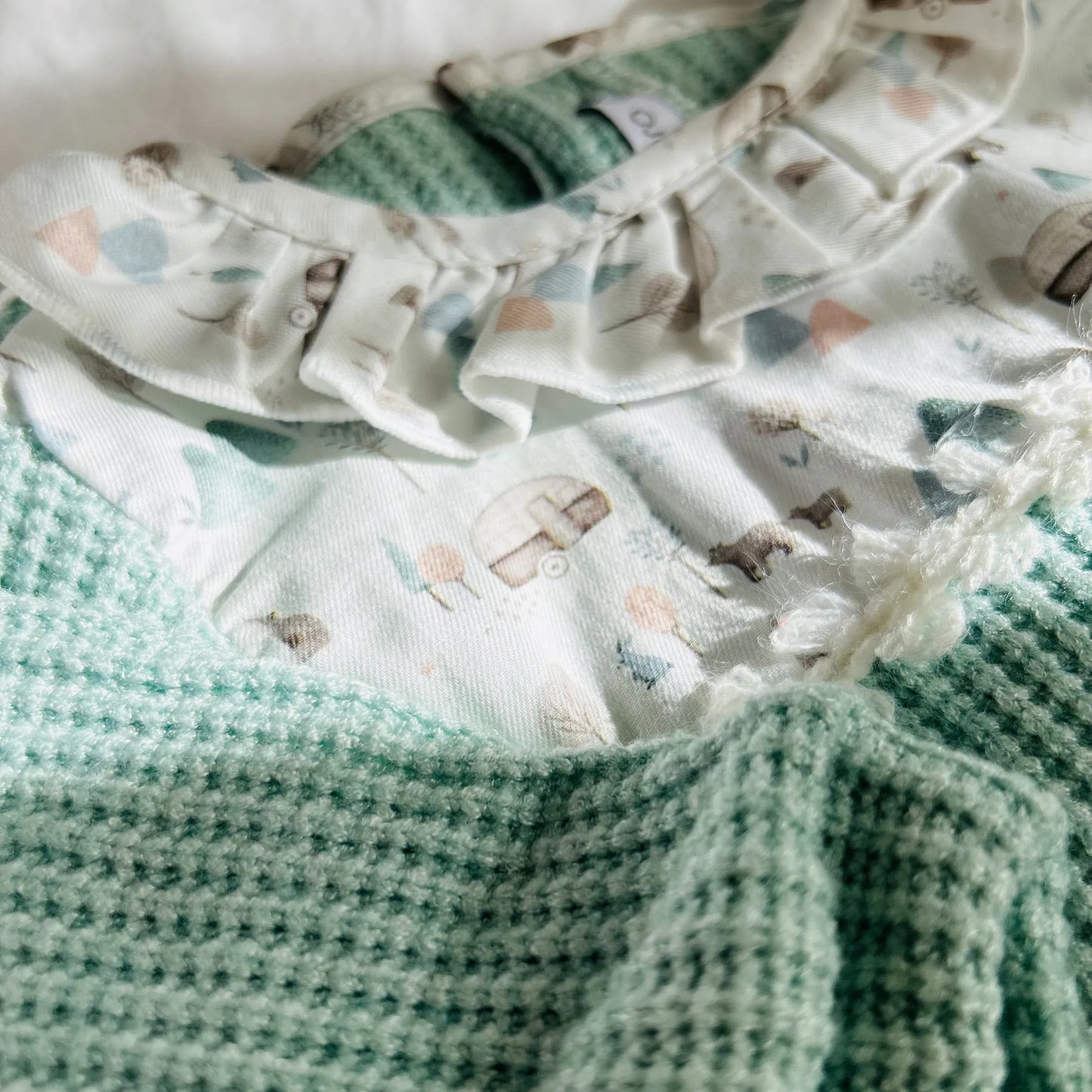 Pormenor de babygrow em tricot com folho na gola e peitilho em contraste verde