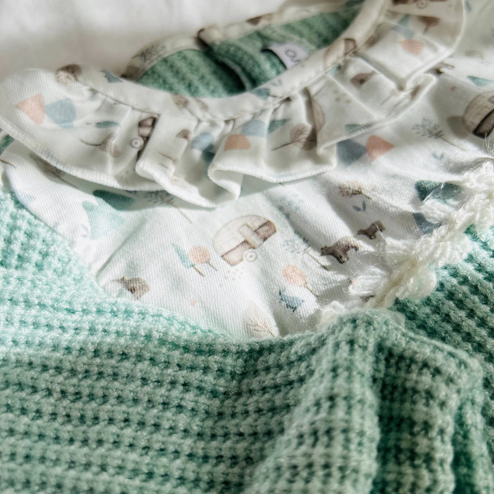 Pormenor de babygrow em tricot com folho na gola e peitilho em contraste verde