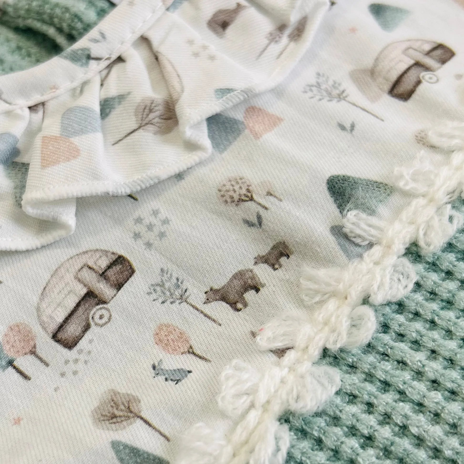 Pormenor de babygrow em tricot com folho na gola e peitilho em contraste verde