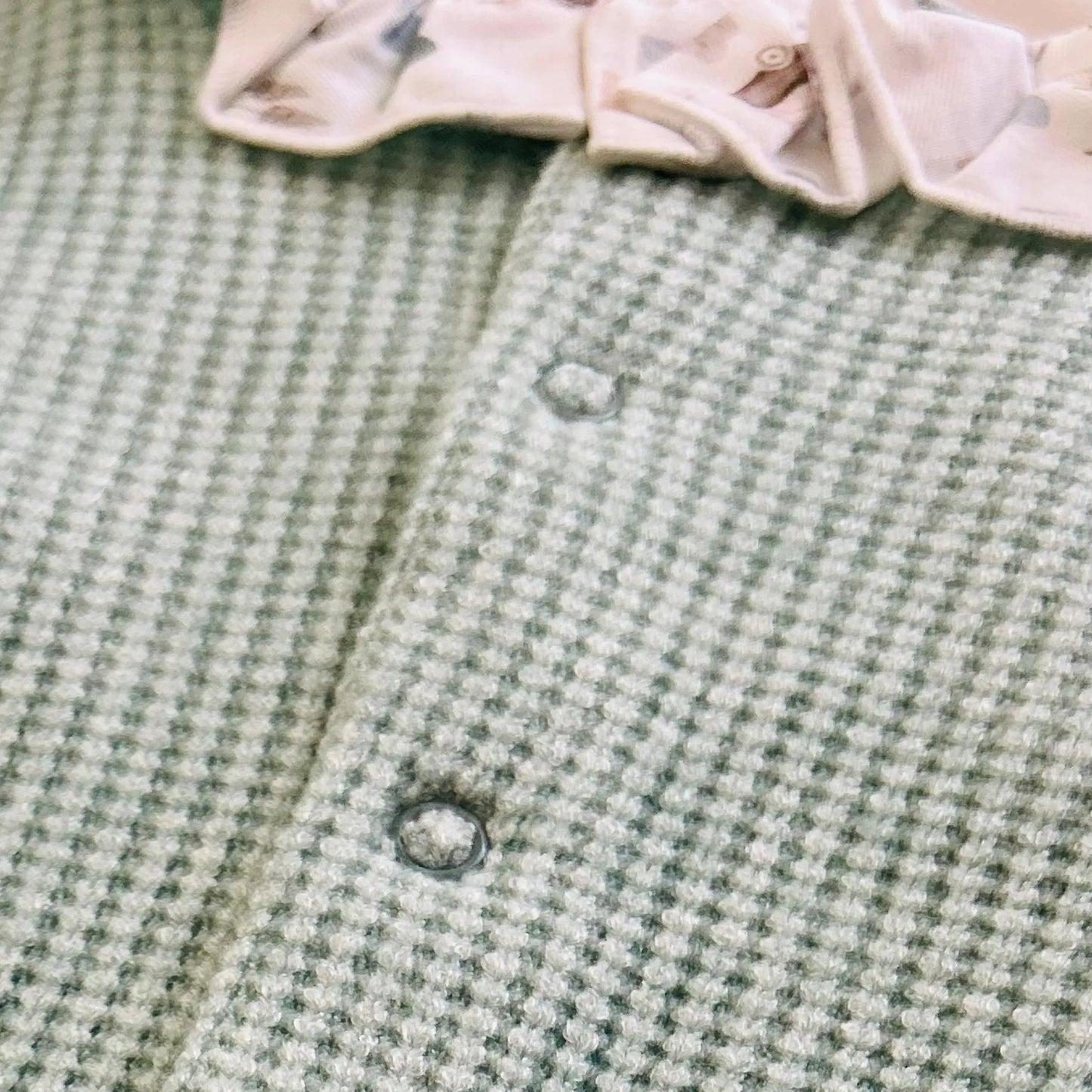Pormenor de babygrow em tricot com folho na gola e peitilho em contraste verde