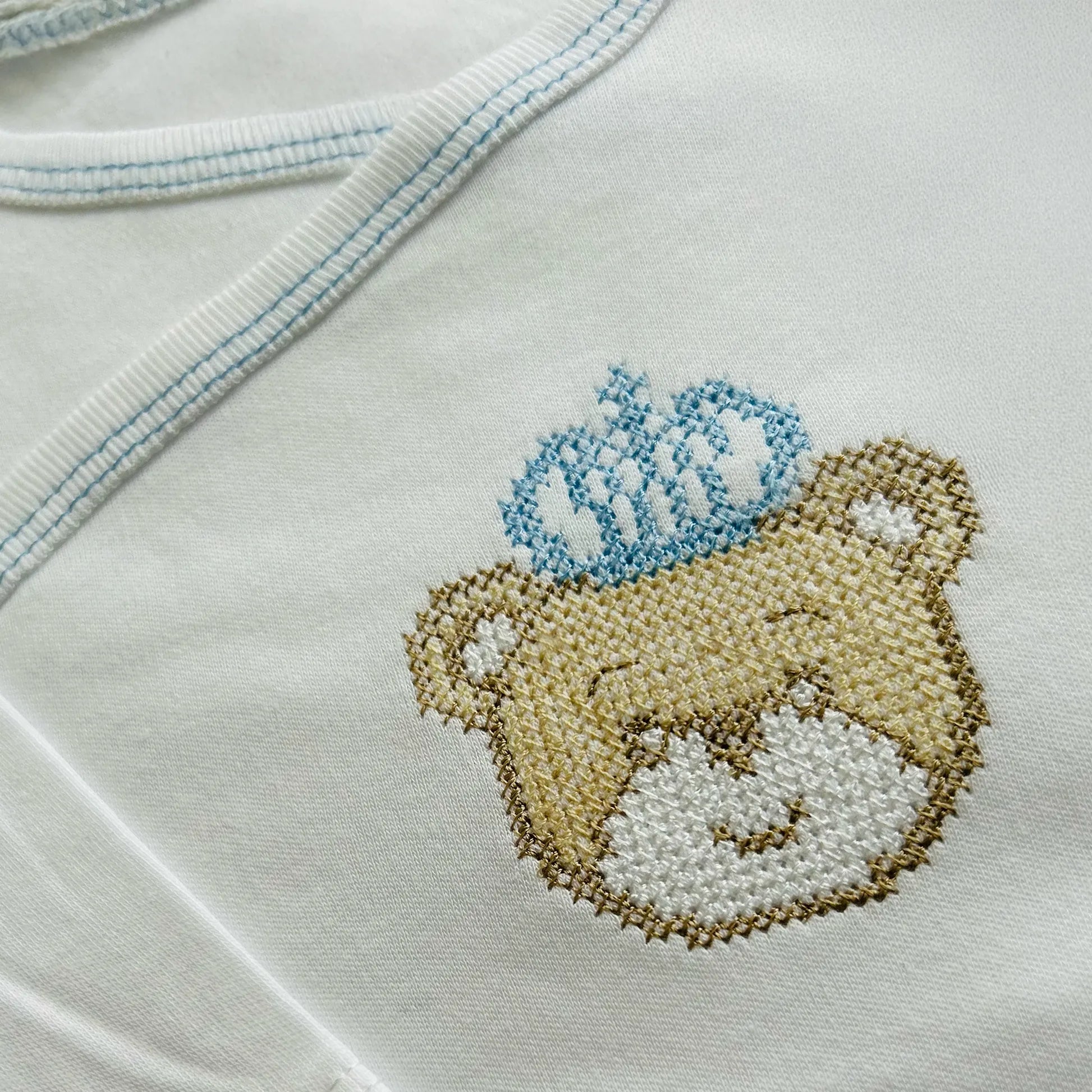 Pormenor de body de trespasse cardado com ursinho bordado em ponto de cruz azul