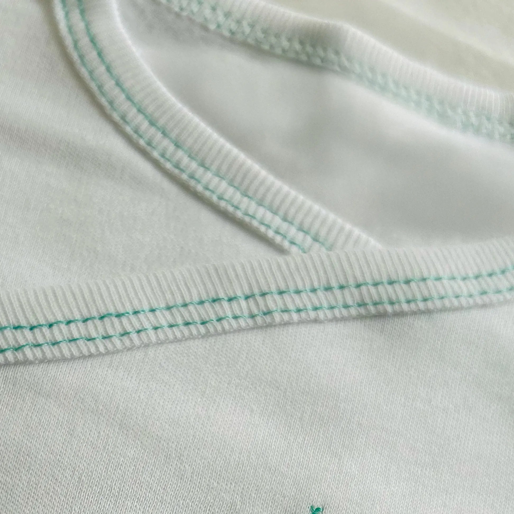 Pormenor de body de trespasse cardado com ursinho bordado em ponto de cruz verde