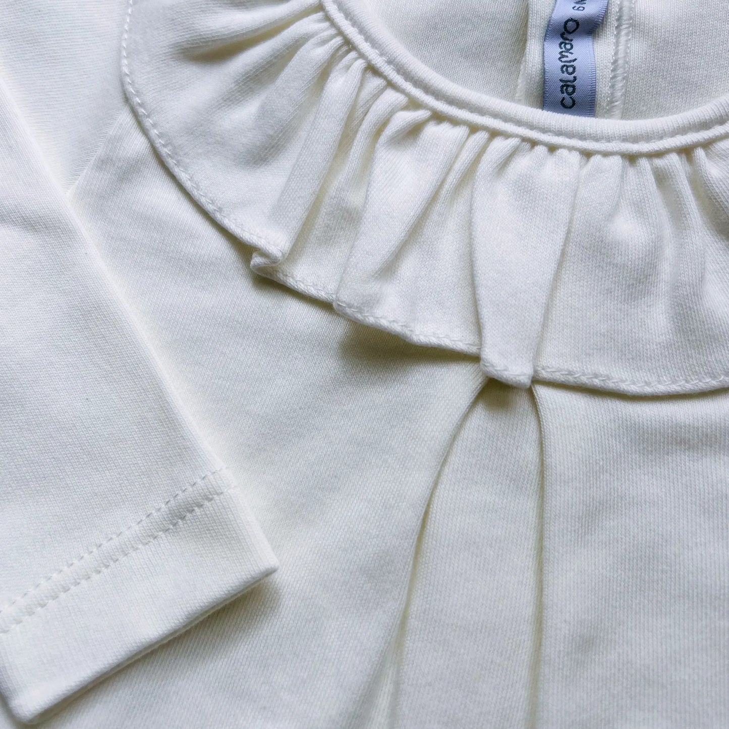 Pormenor de camisola de menina com folho na gola e prega na frente pérola