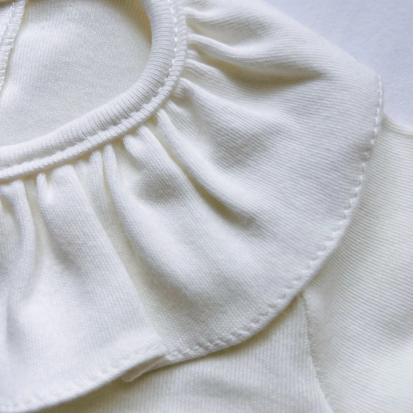 Pormenor de camisola de menina com folho na gola e prega na frente pérola