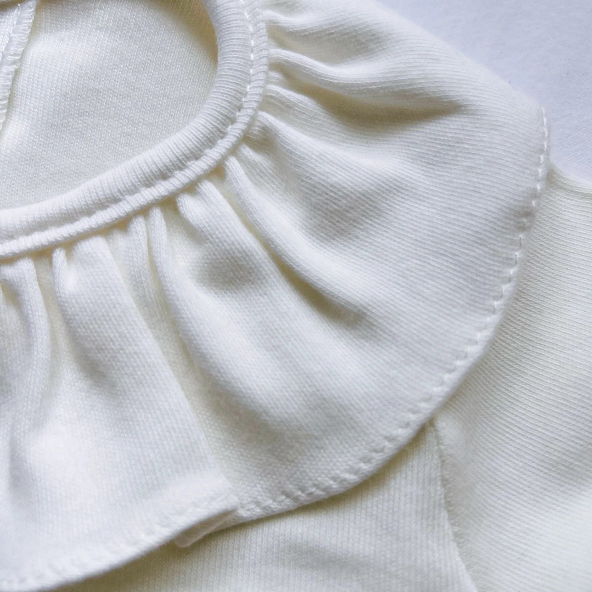 Pormenor de camisola de menina com folho na gola e prega na frente pérola