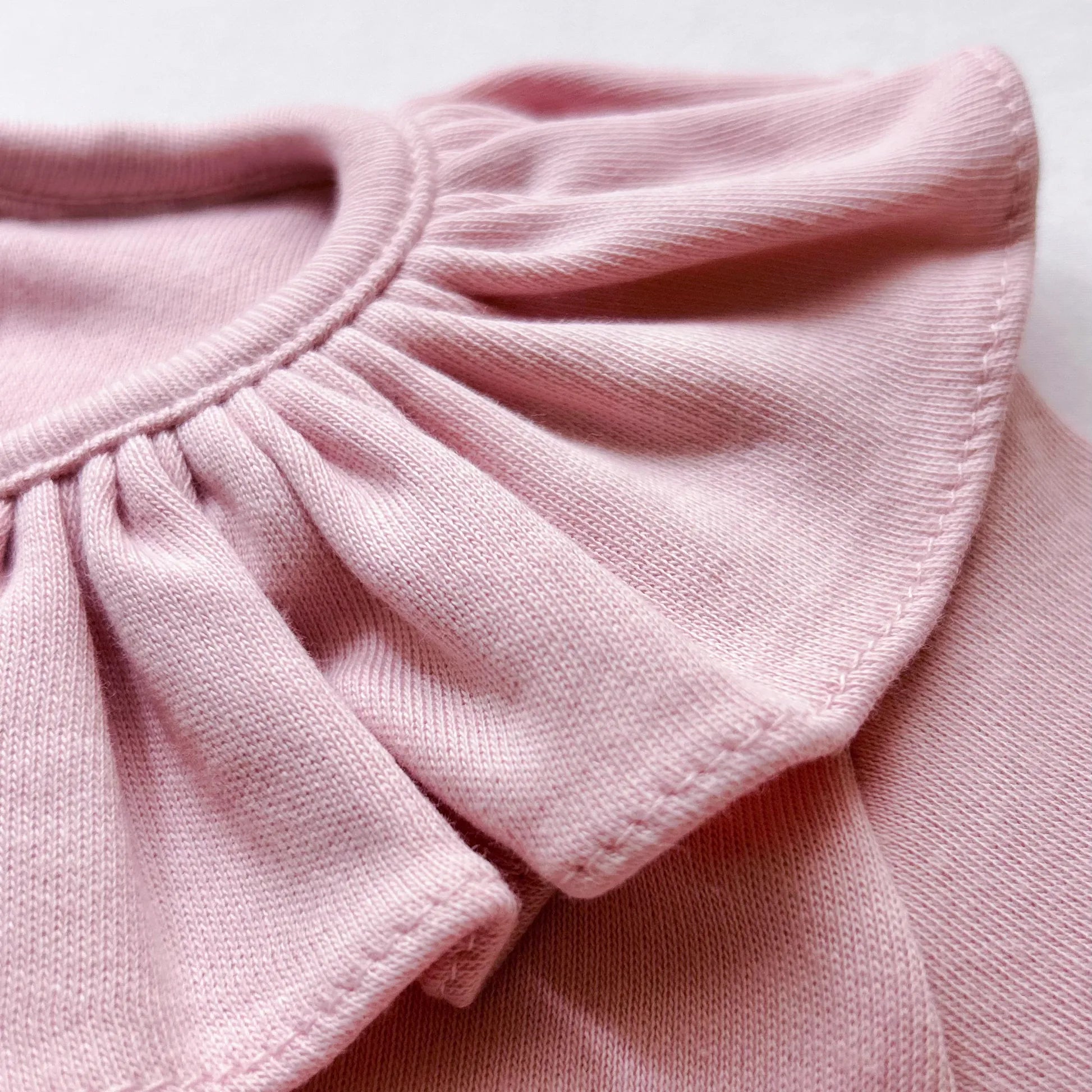 Pormenor de camisola de menina com folho na gola e prega na frente rosa