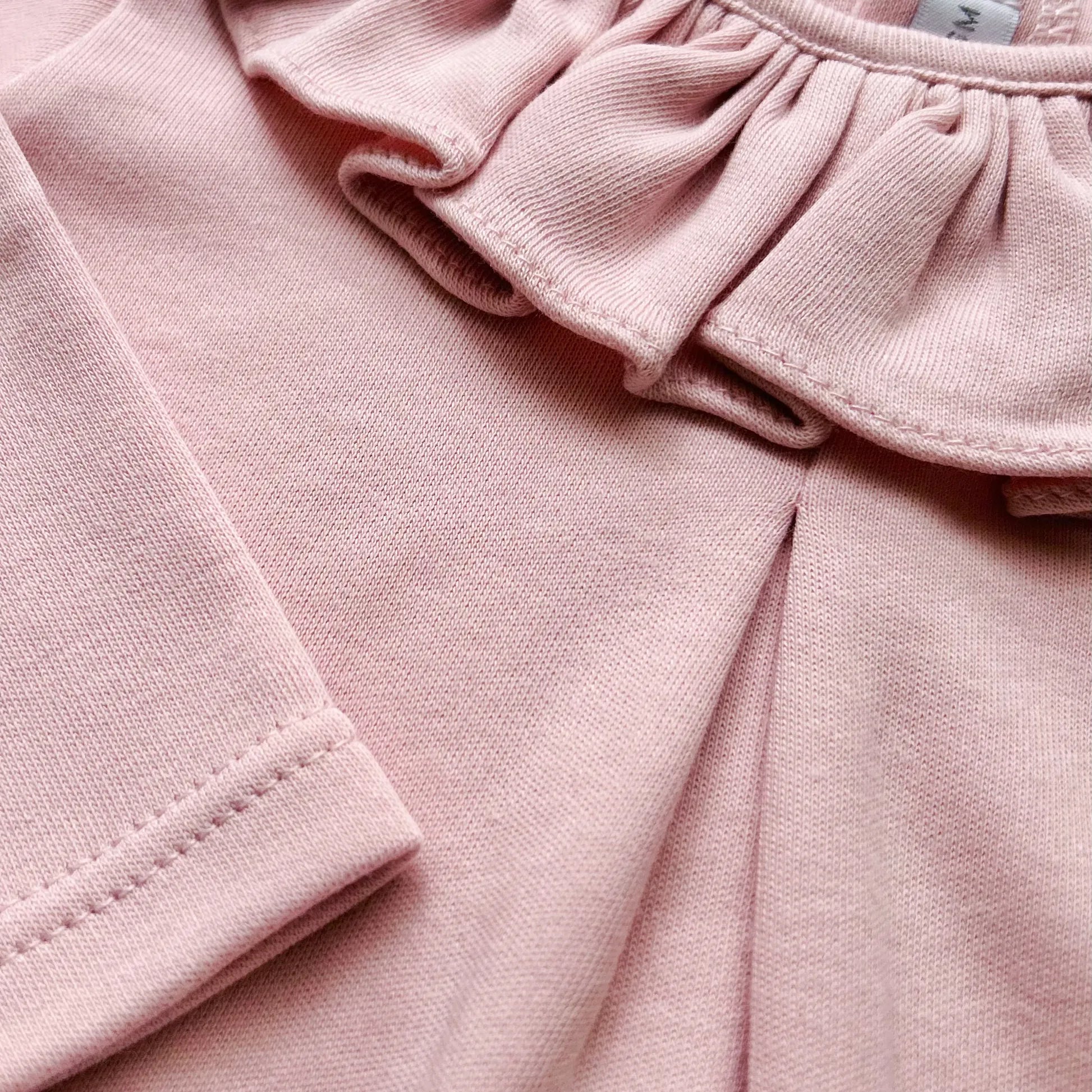 Pormenor de camisola de menina com folho na gola e prega na frente rosa