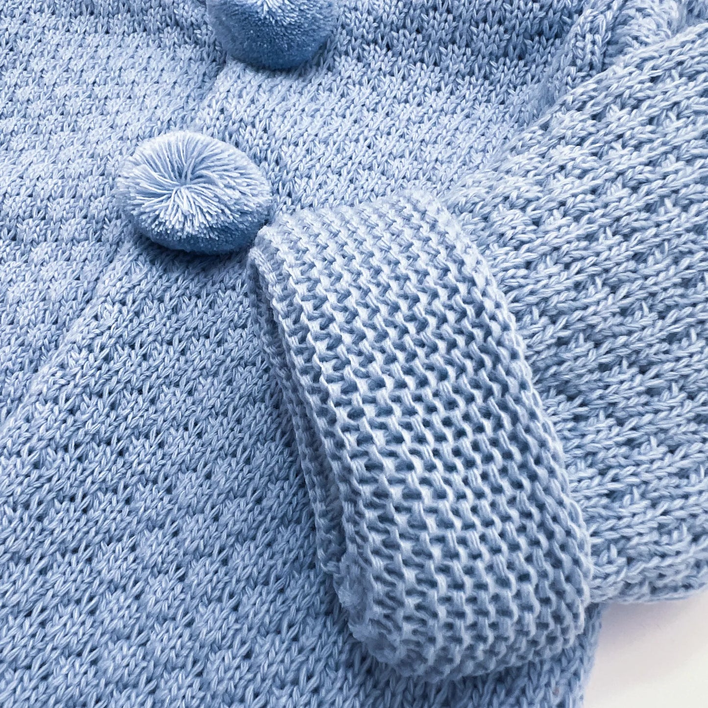 Pormenor de casaco de malha com capuz com pompons na zona dos botões azul