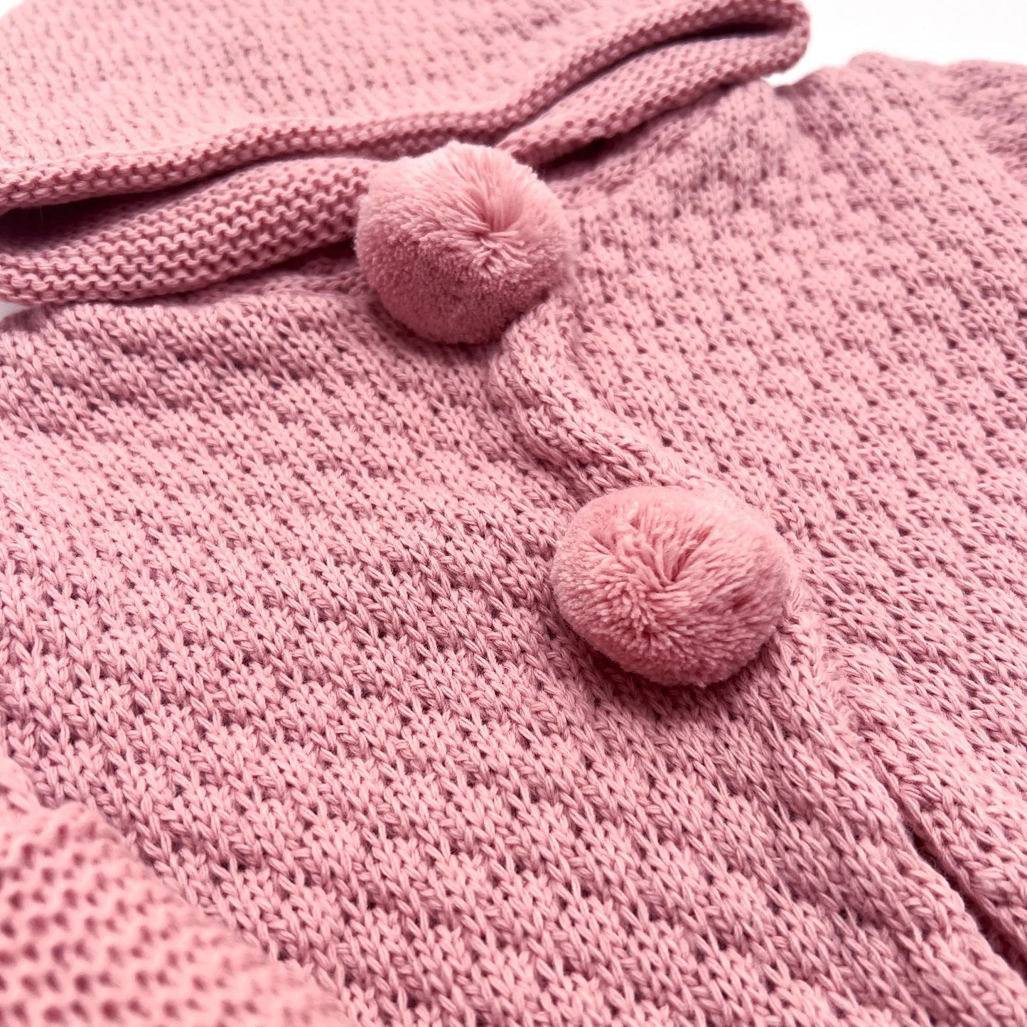 Pormenor de casaco de malha com capuz com pompons na zona dos botões rosa